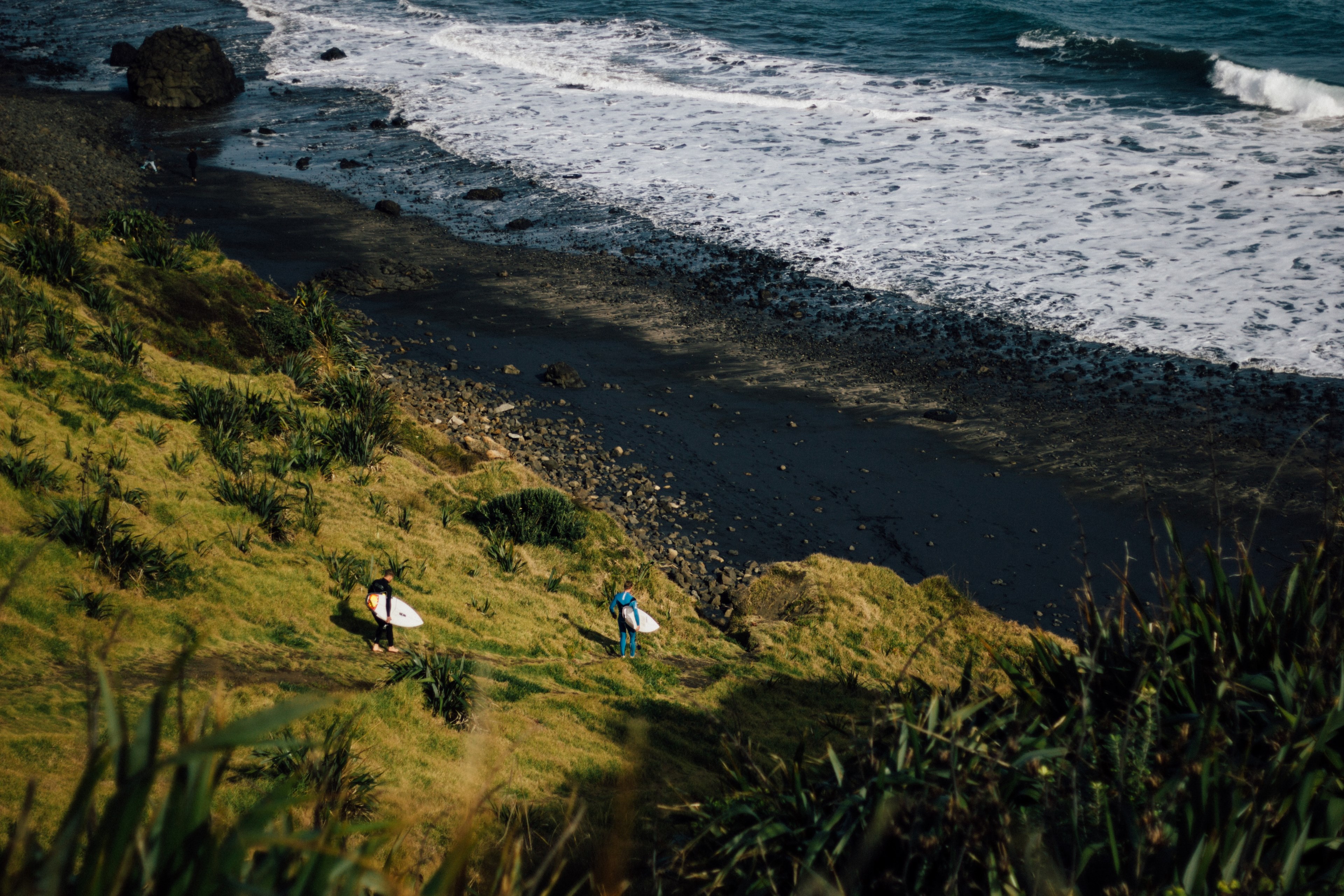 two men carrying surfboards walking down a grassy dune towards the beach and sea at maori bay, heading for the sea 4k, HD Wallpaper