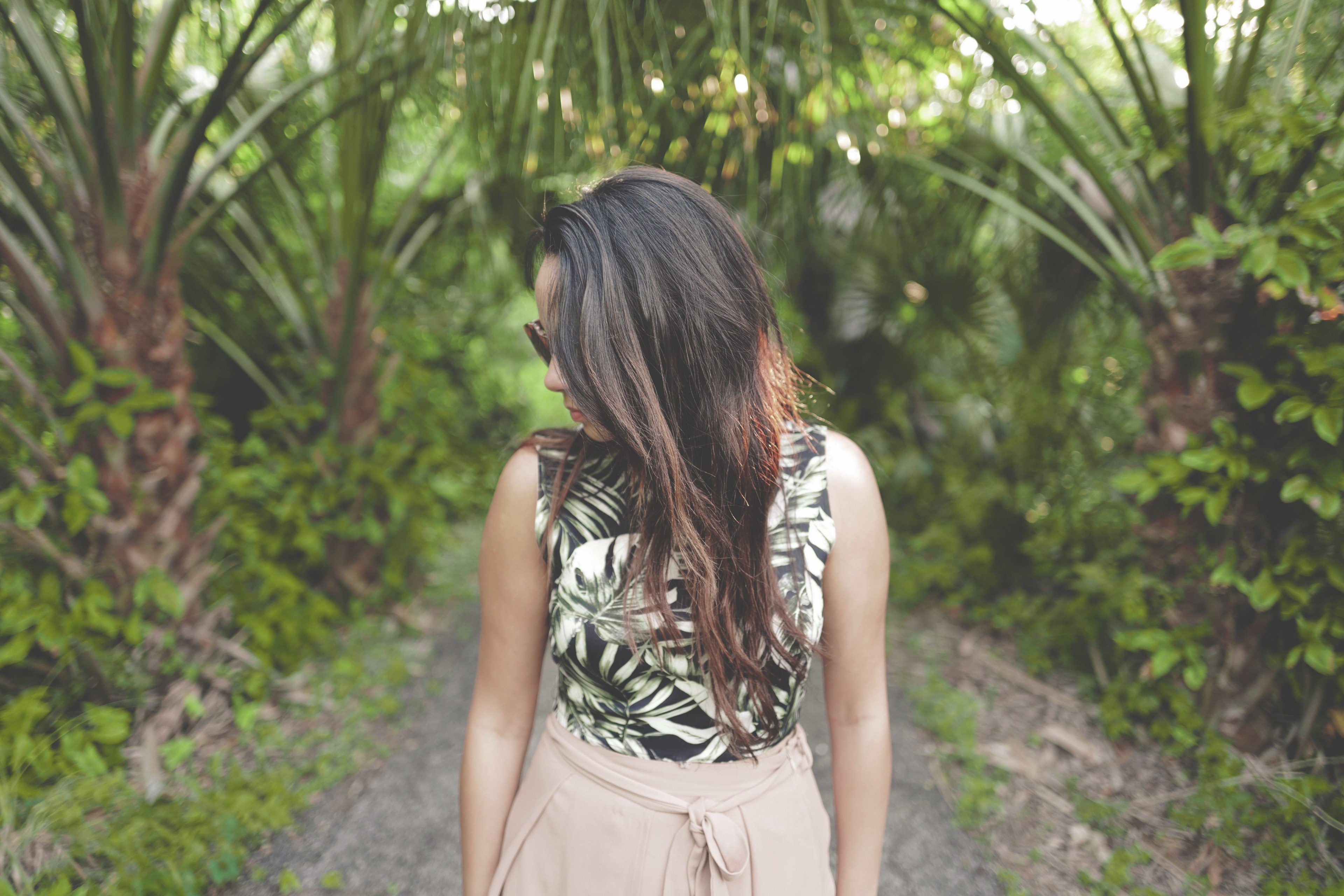 a young dark haired woman in sunglasses tilting her head to the side in a tropical setting, walking under the palm trees 4k, HD Wallpaper
