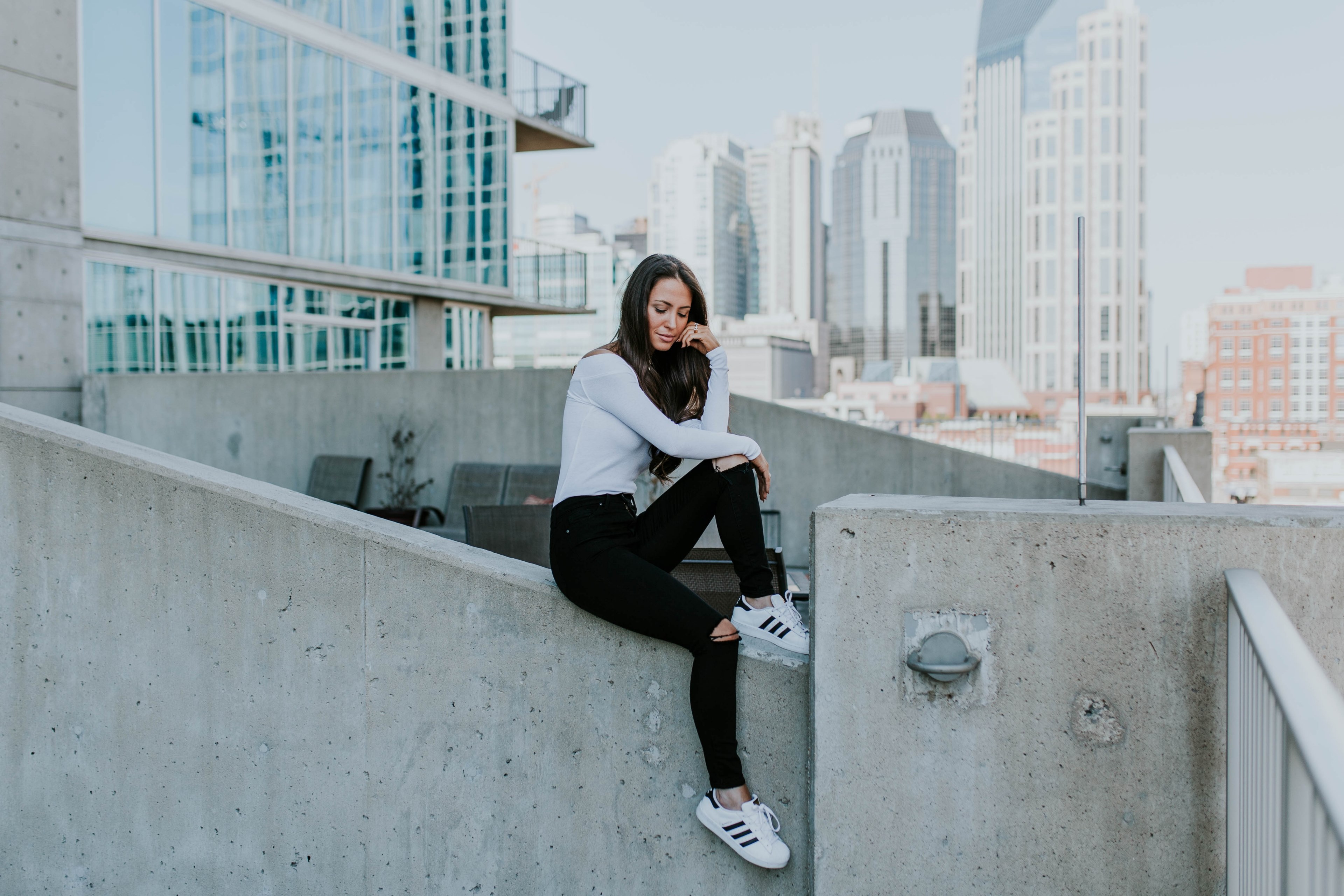 a young woman in ripped jeans posing while sitting on a concrete ledge in a city, woman in front of skyline 4k, HD Wallpaper