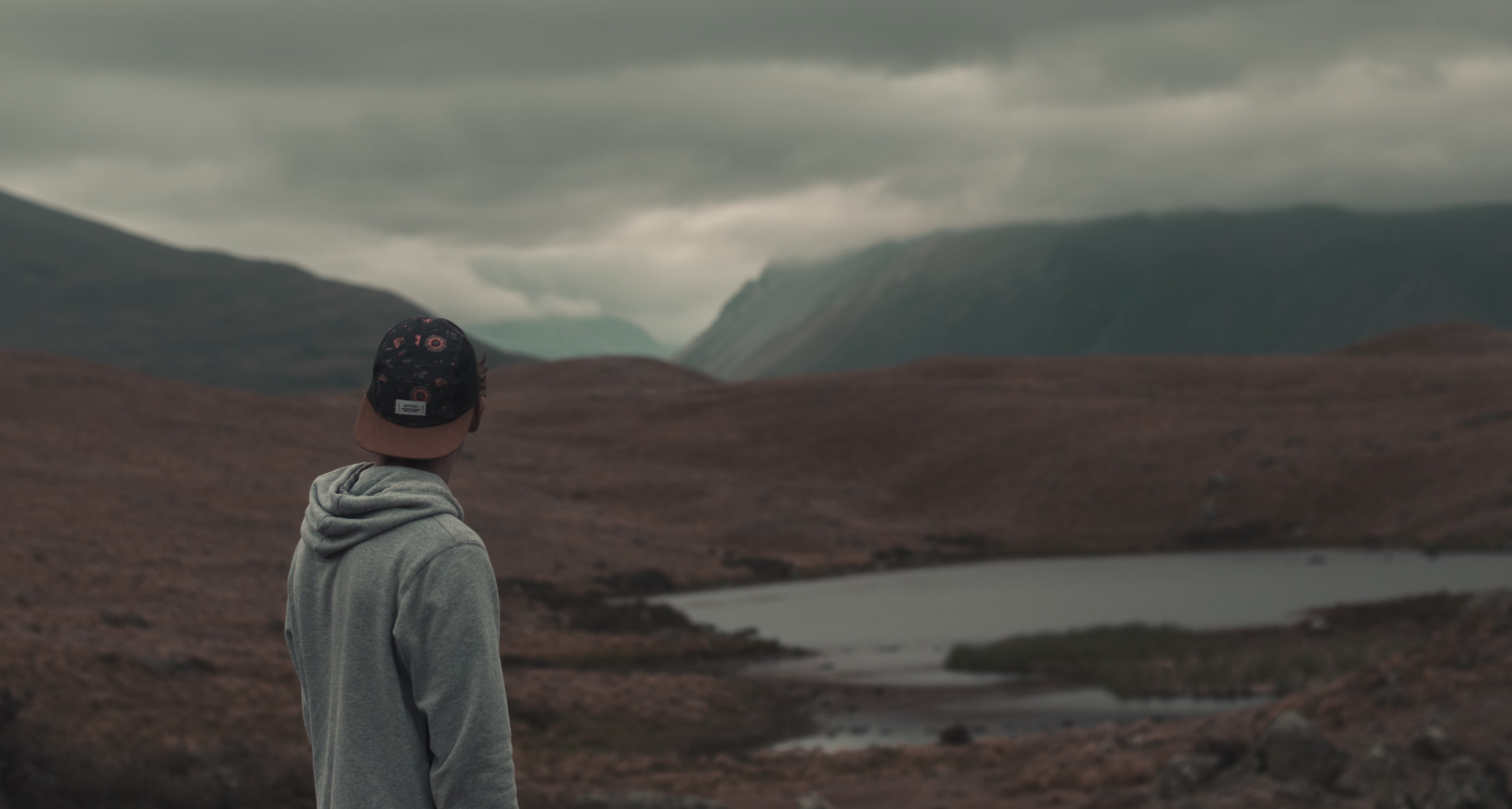 a man wearing a hat and a hoodie standing in front of lake alexandrina in a cloudy weather, man standing by lake 4k, HD Wallpaper