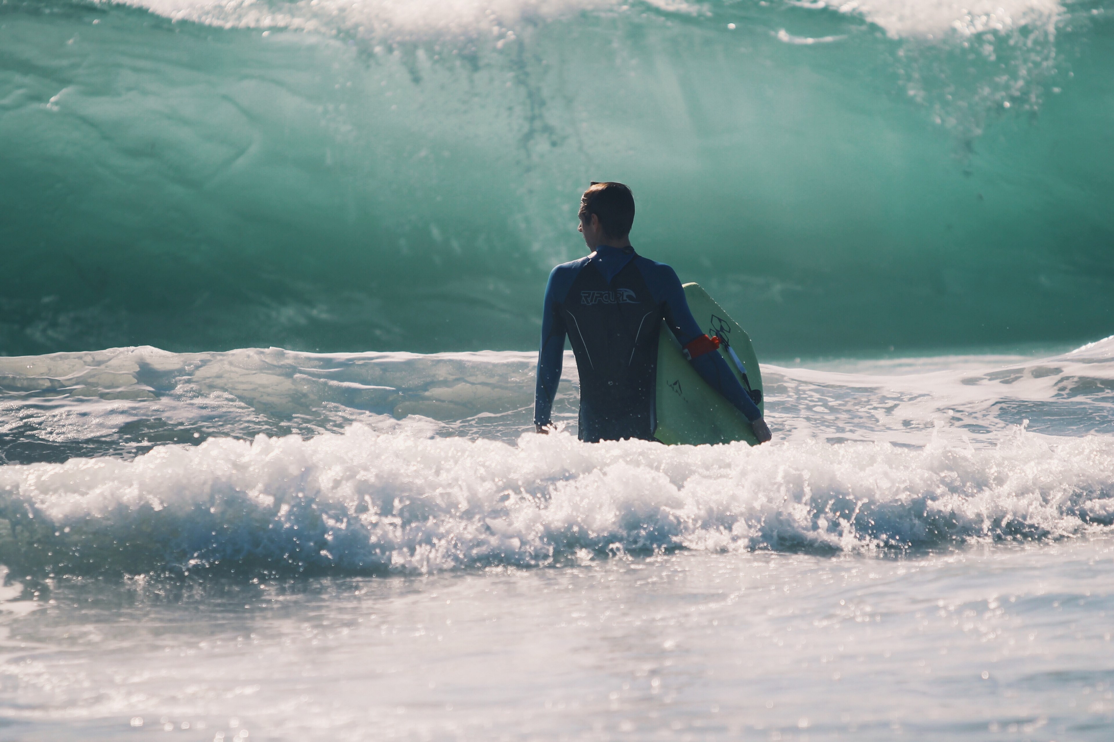 a man in a wetsuit stood in the sea holding his board looking out at a massive onrushing wave, surfer watching the onrushing wave 4k, HD Wallpaper