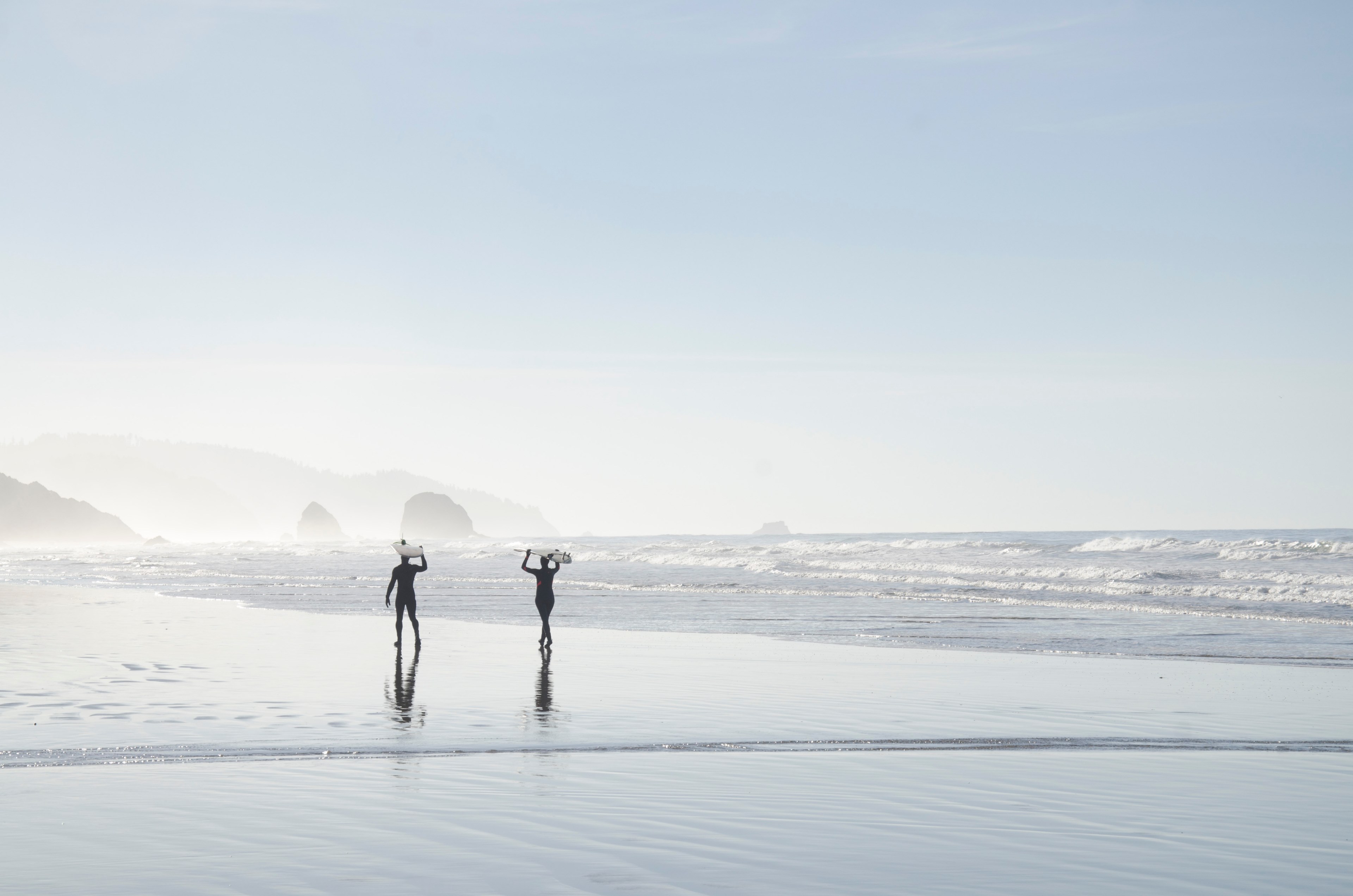silhouettes of two people carrying surfboards above their heads on a wet beach, surfer silhouettes on cannon beach 4k, HD Wallpaper
