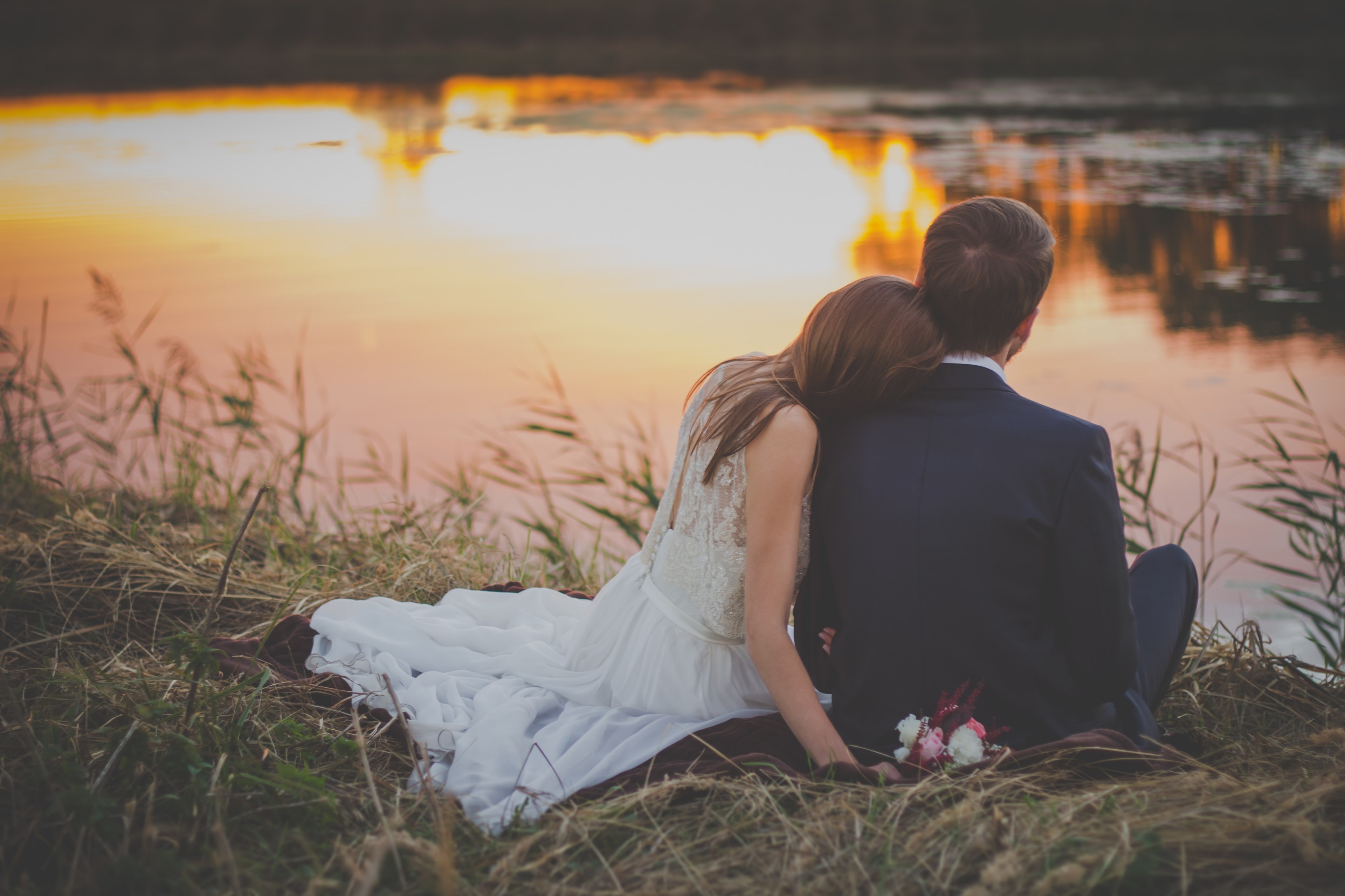 bride rests head on groom while looking at a pond during sunset, bride and groom sit by pond 4k, HD Wallpaper