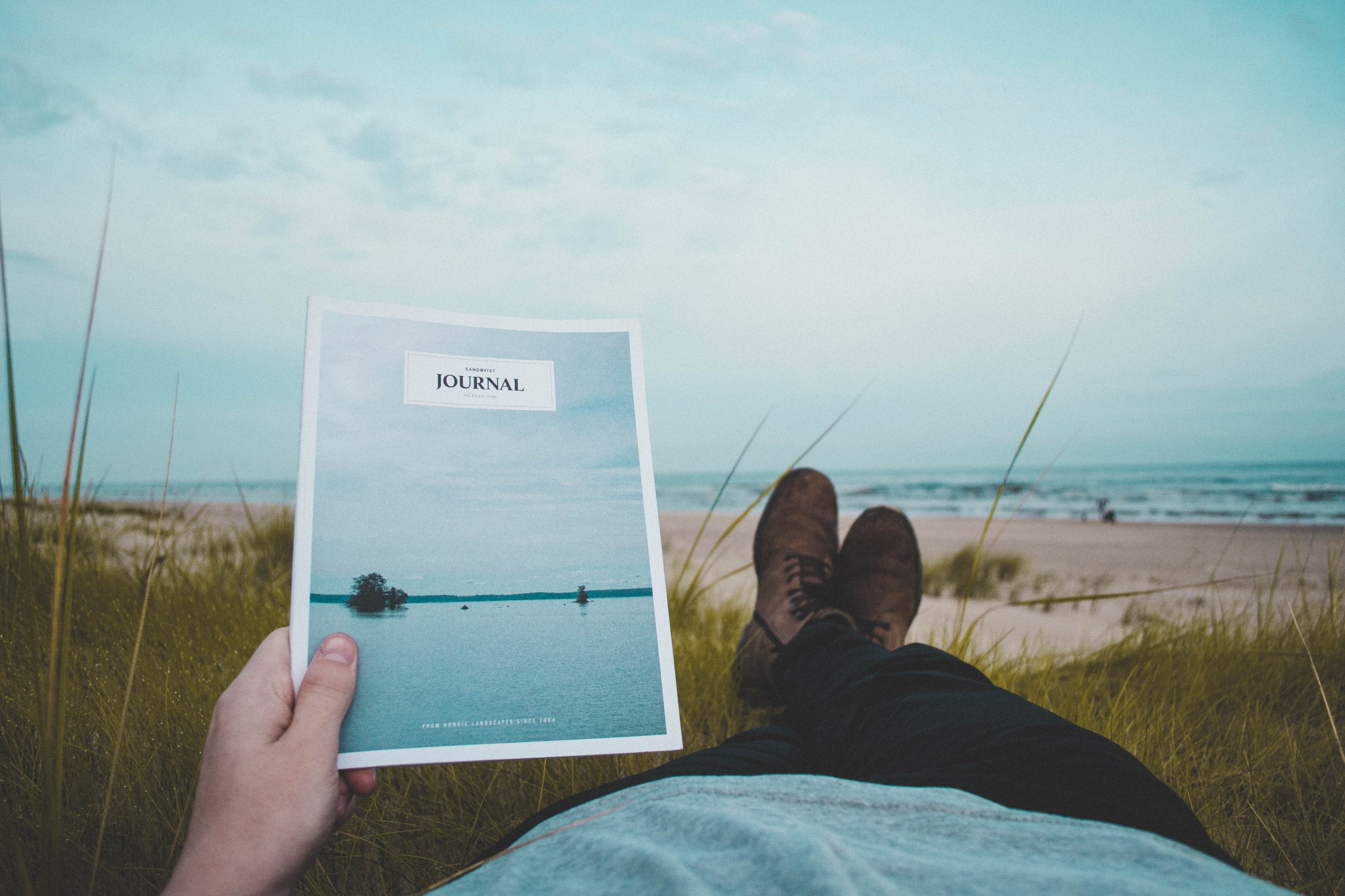 person lying on the grass at the sand beach holding a magazine journal, person holding a journal 4k, HD Wallpaper
