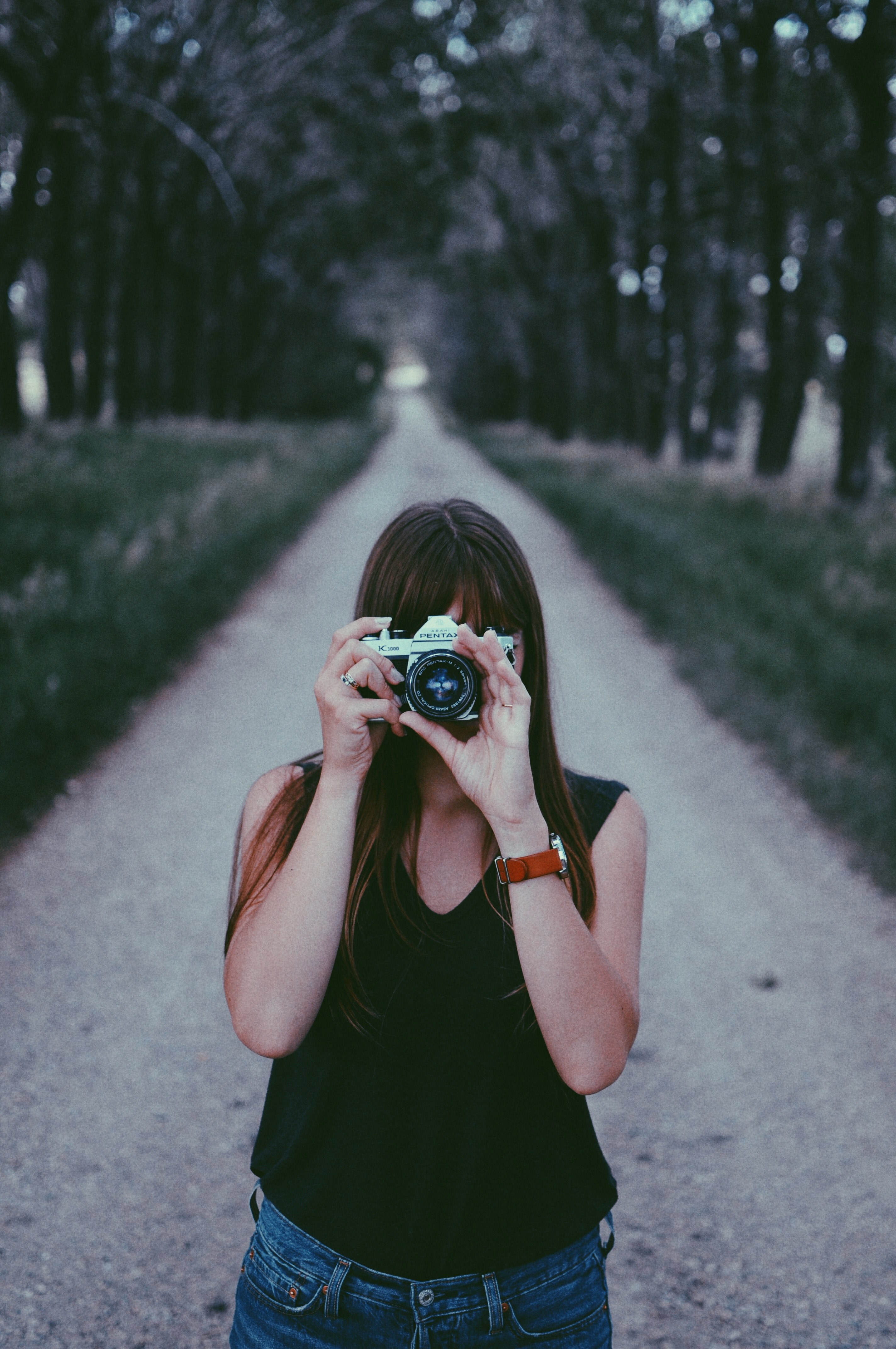 a woman standing in the middle of a dirt road and taking a photo with a camera, photographer on a dirt road 4k, Phone HD Wallpaper
