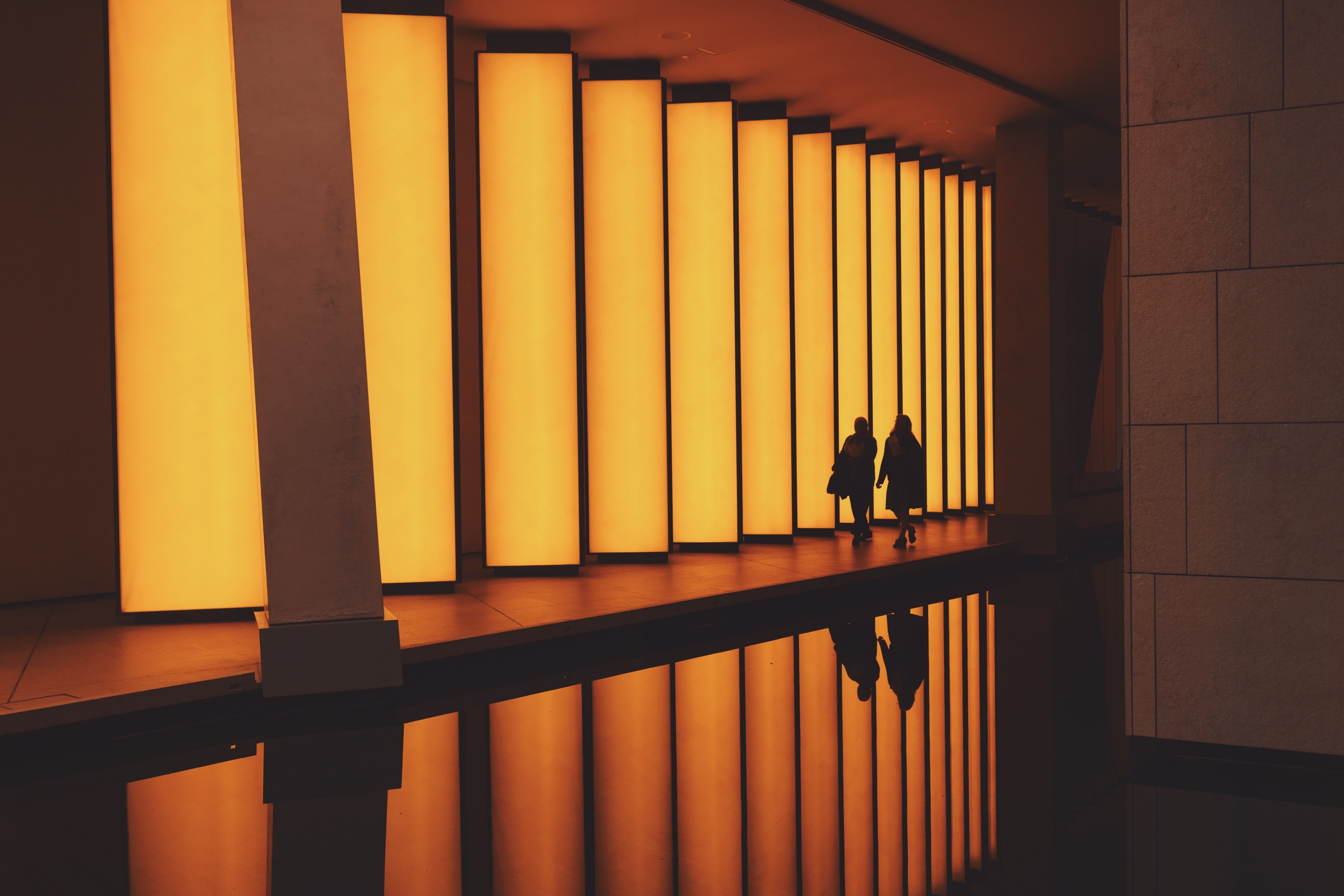 two silhouettes of women walking through an orange lighted architectural spot, orange columns and silhouettes 4k, HD Wallpaper