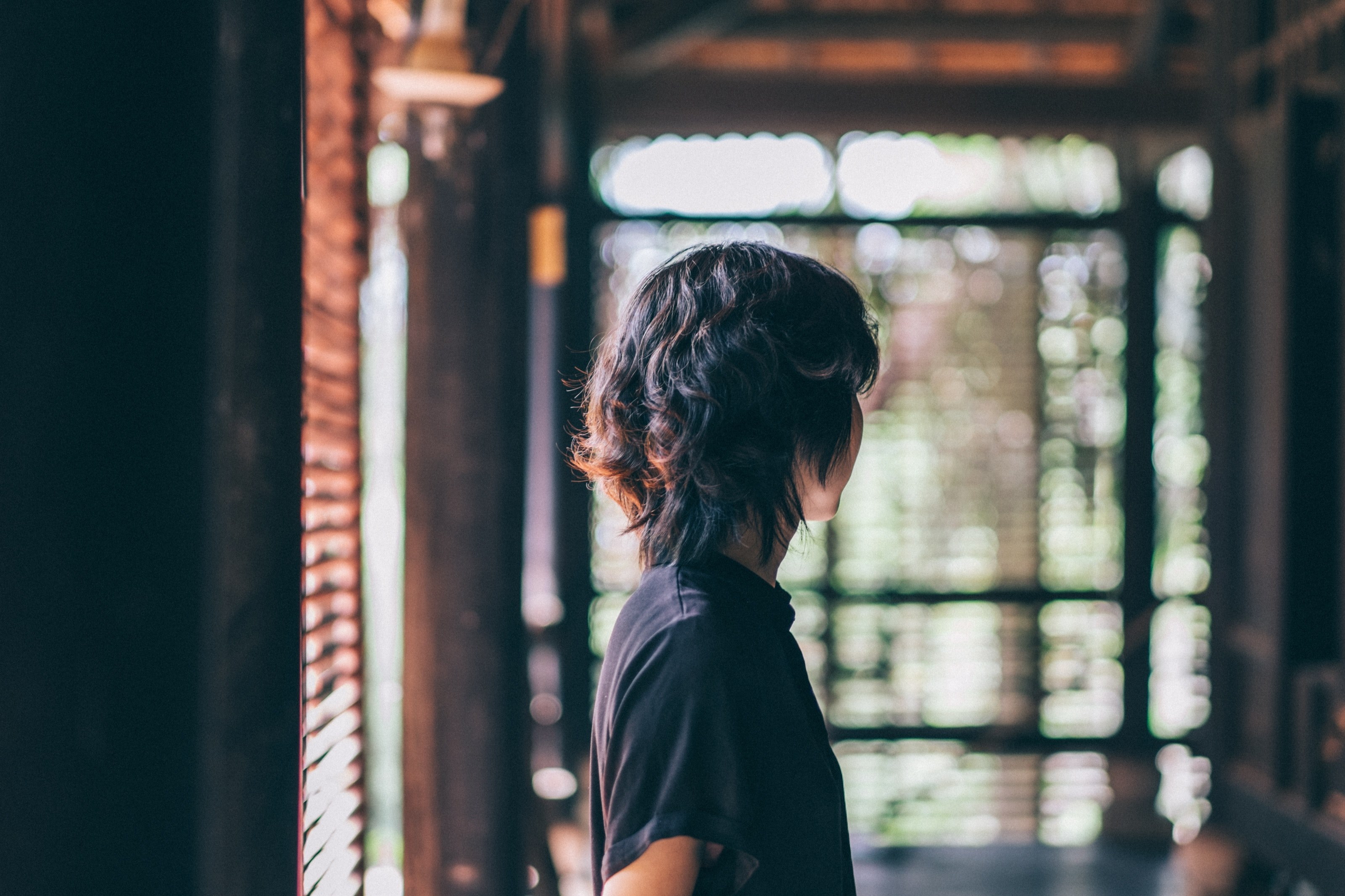 a person stands in a hallway facing away toward a window with open blinds, woman looking out blinds 4k, HD Wallpaper
