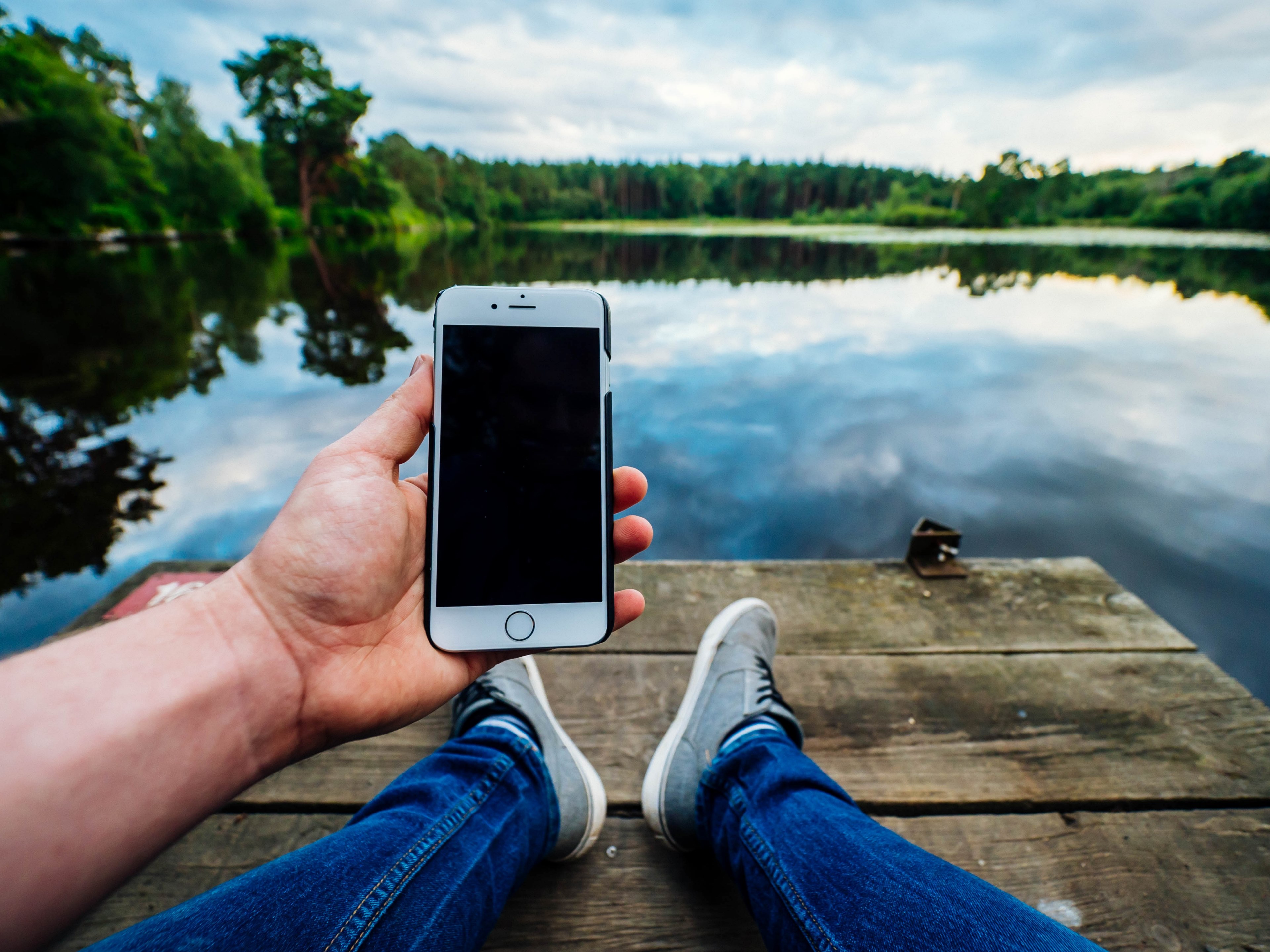 a person wearing jeans and sneakers holding an iphone cellphone by a lake at henley park, henley park hangouts 4k, HD Wallpaper