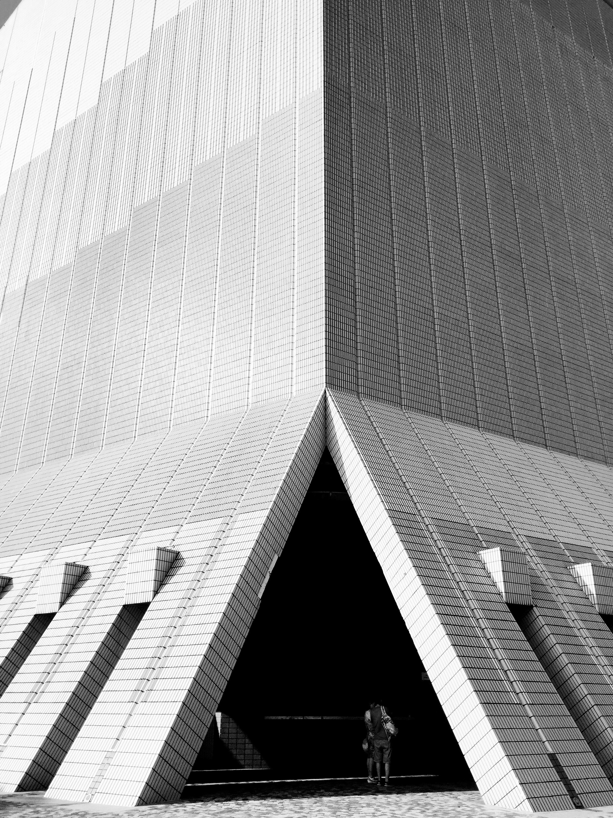 a black and white shot of a triangular opening at the bottom of a modern building facade, hongkong 4k, Phone HD Wallpaper