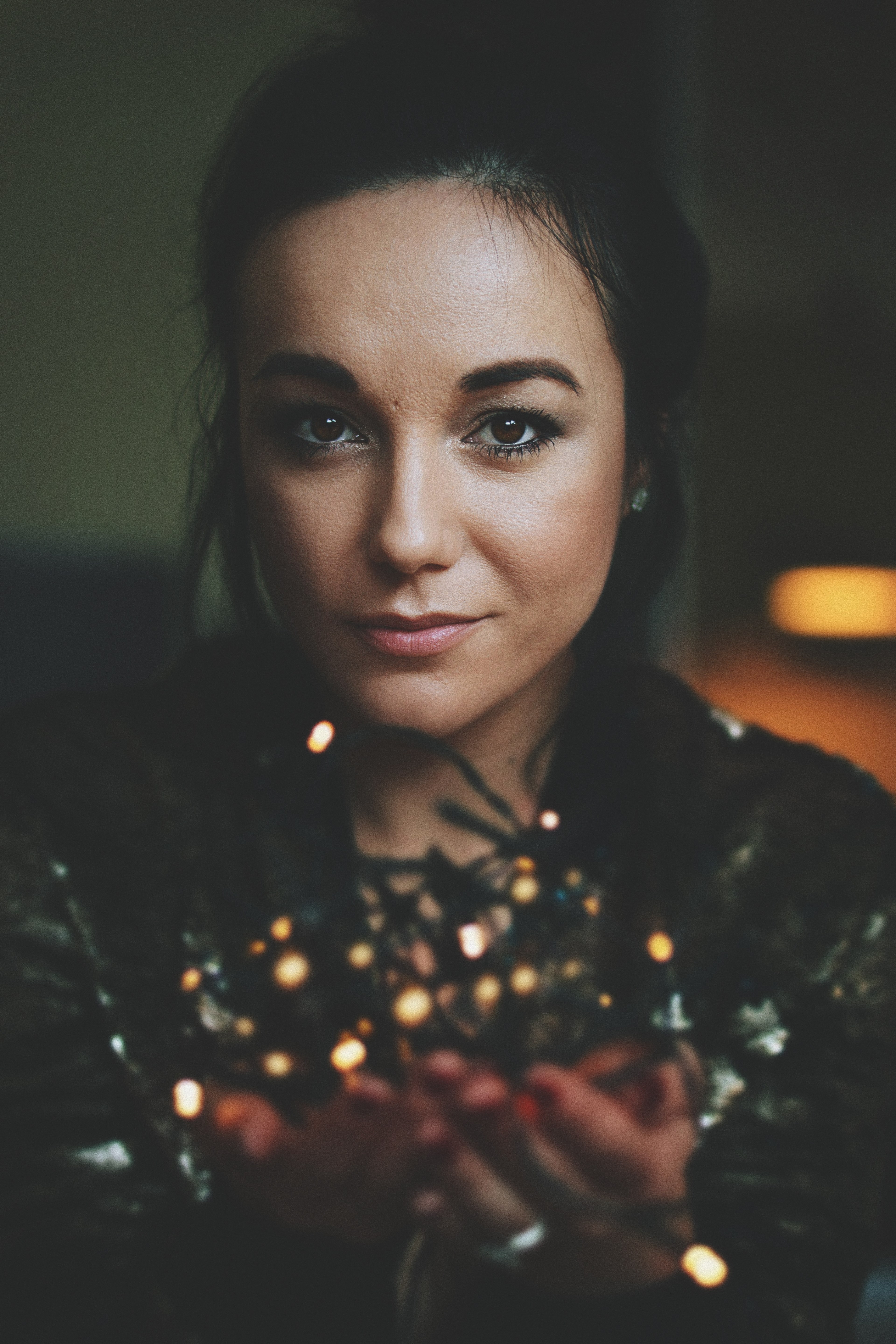 a woman with a serious expression holds up a string of christmas lights in her palms, dinara 4k, Phone HD Wallpaper