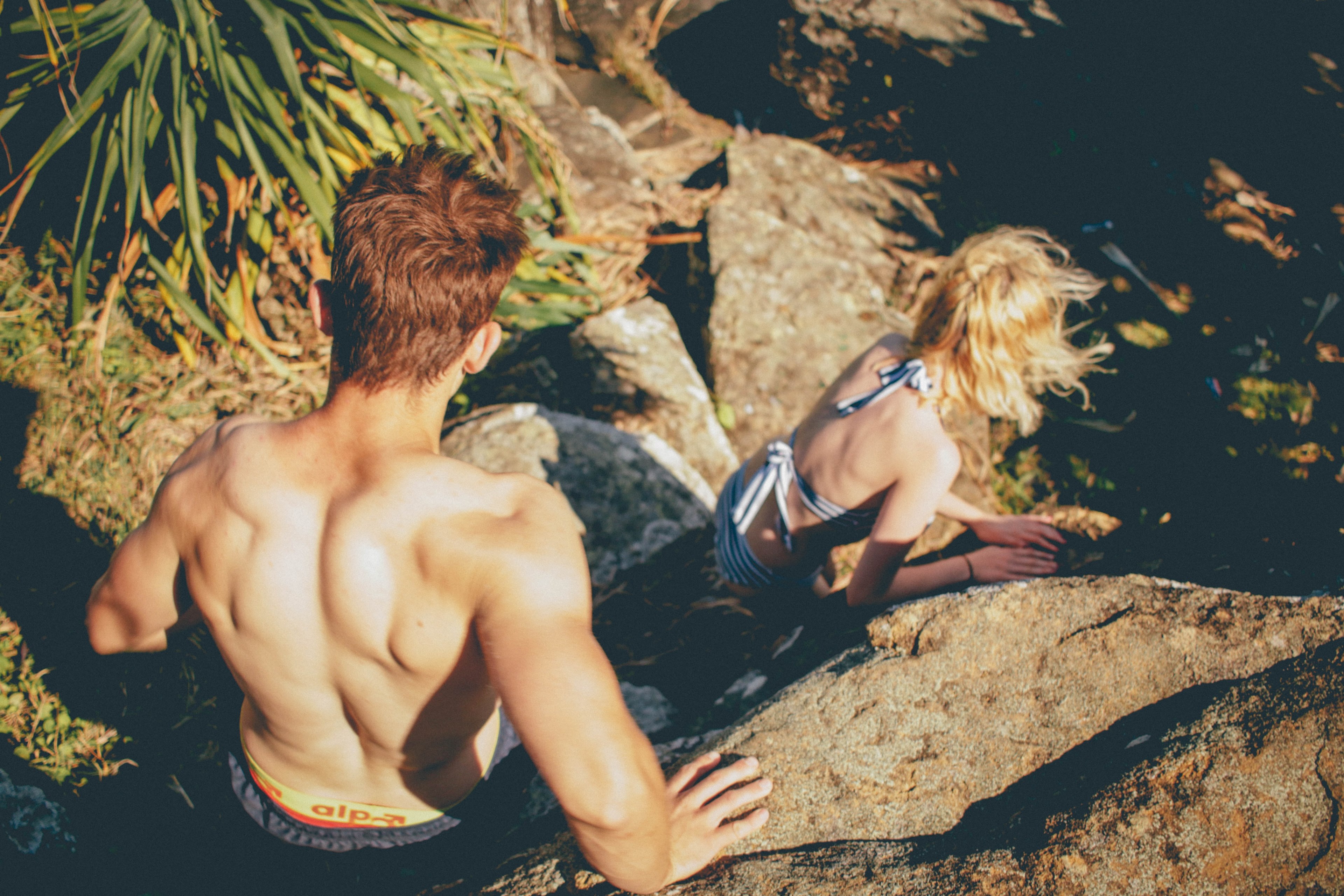 couple in swimwear climbing down the rocky cliff at kings beach, couple climbing down the cliff 4k, HD Wallpaper