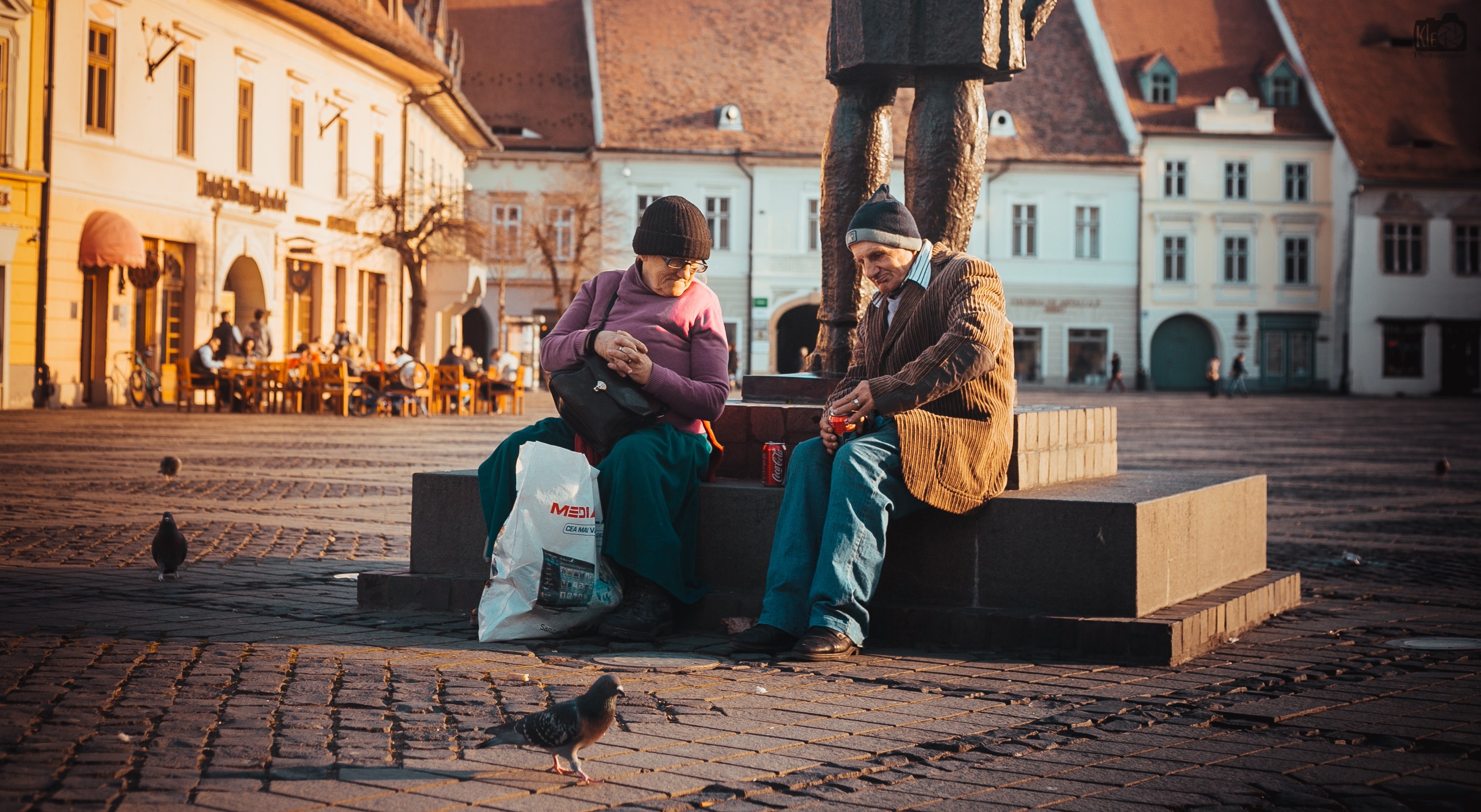 two smiling people sitting with drinks and shopping bags aside a statue in a city square, people sitting in city square 4k, HD Wallpaper