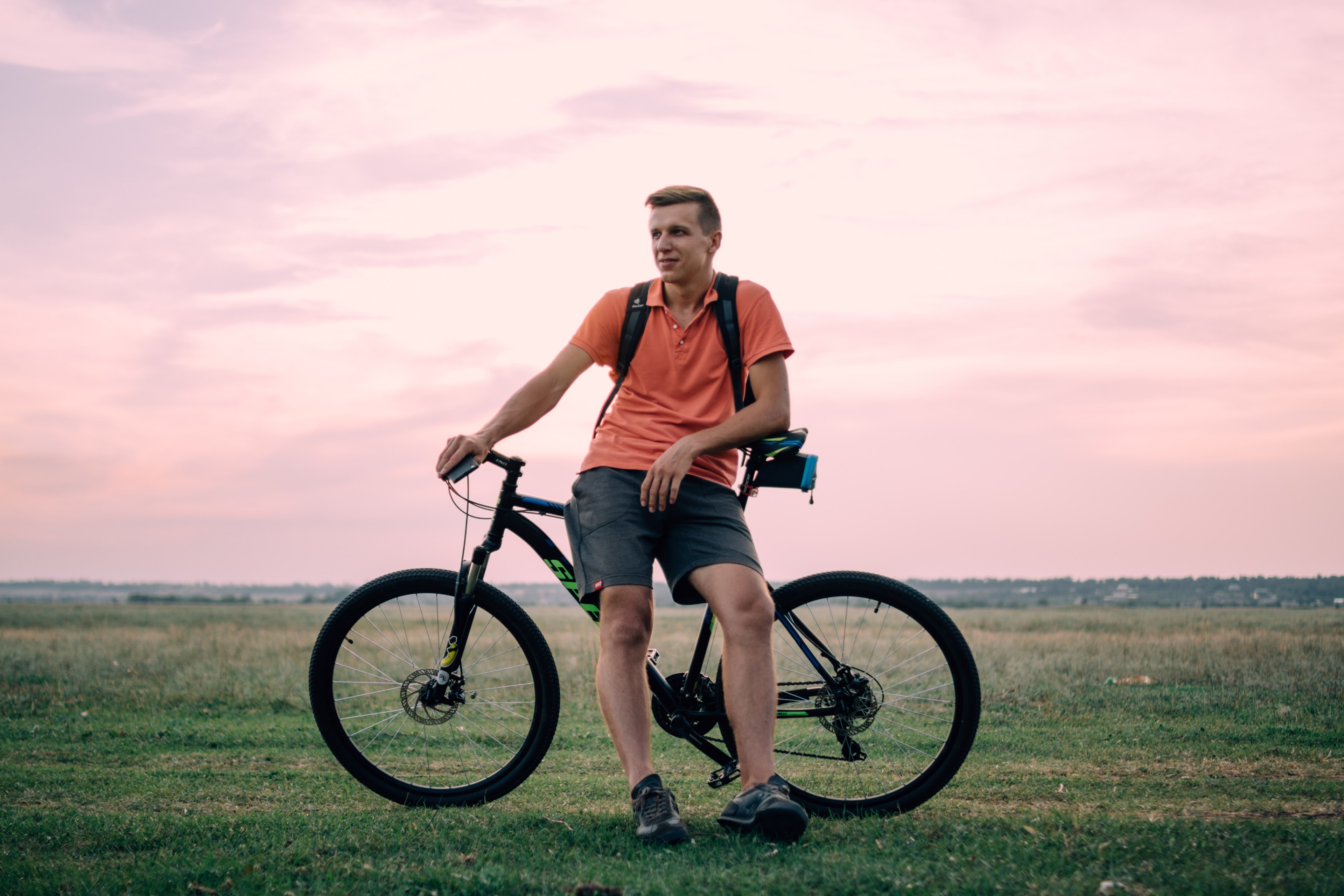 a man standing poised in a pink shirt in front of his bicycle in the country grass, man standing with bike 4k, HD Wallpaper