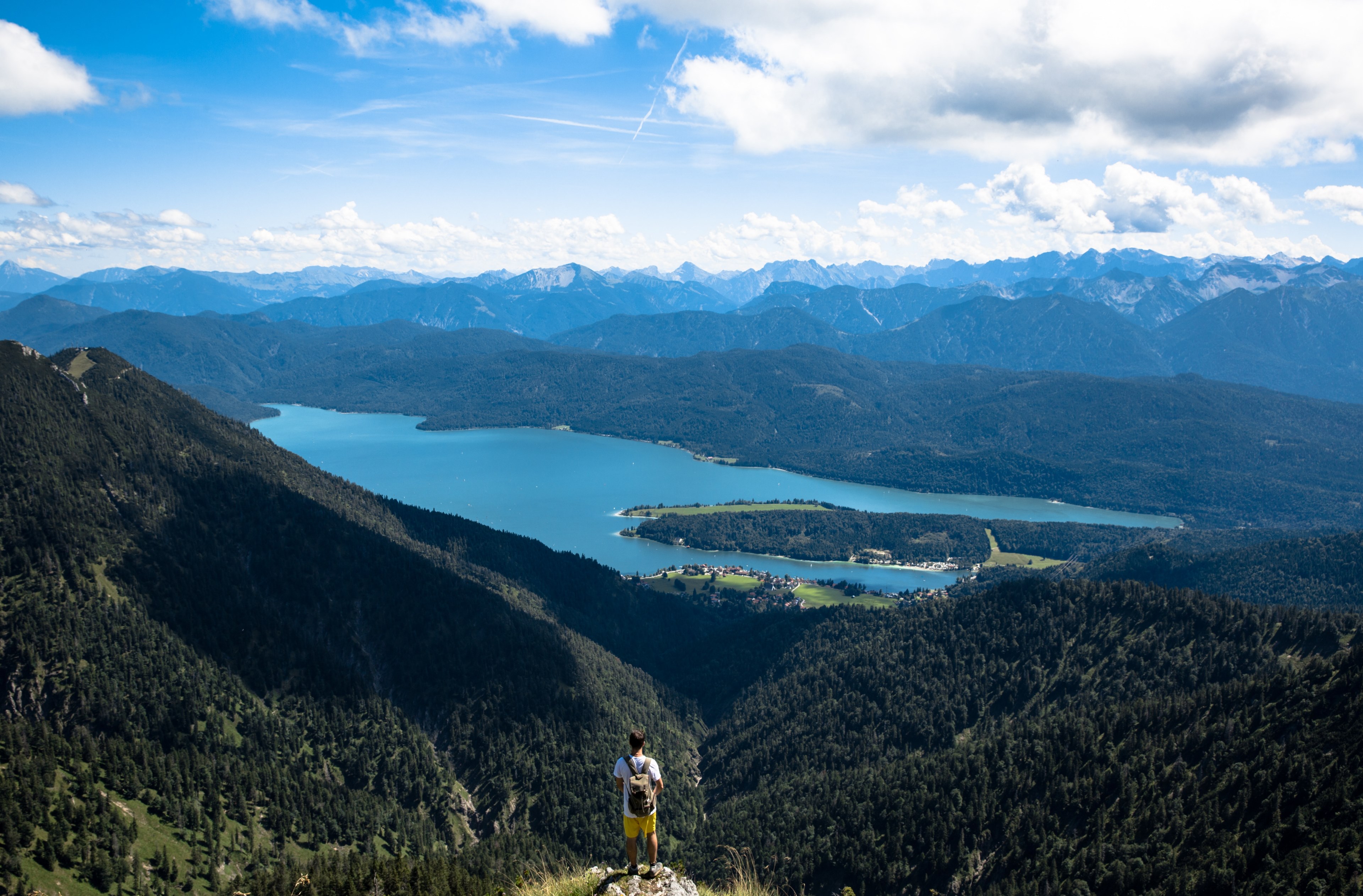 a male backpacker standing on a rock overlooking a mountain valley and a blue lake, high above the mountain valley 4k, HD Wallpaper