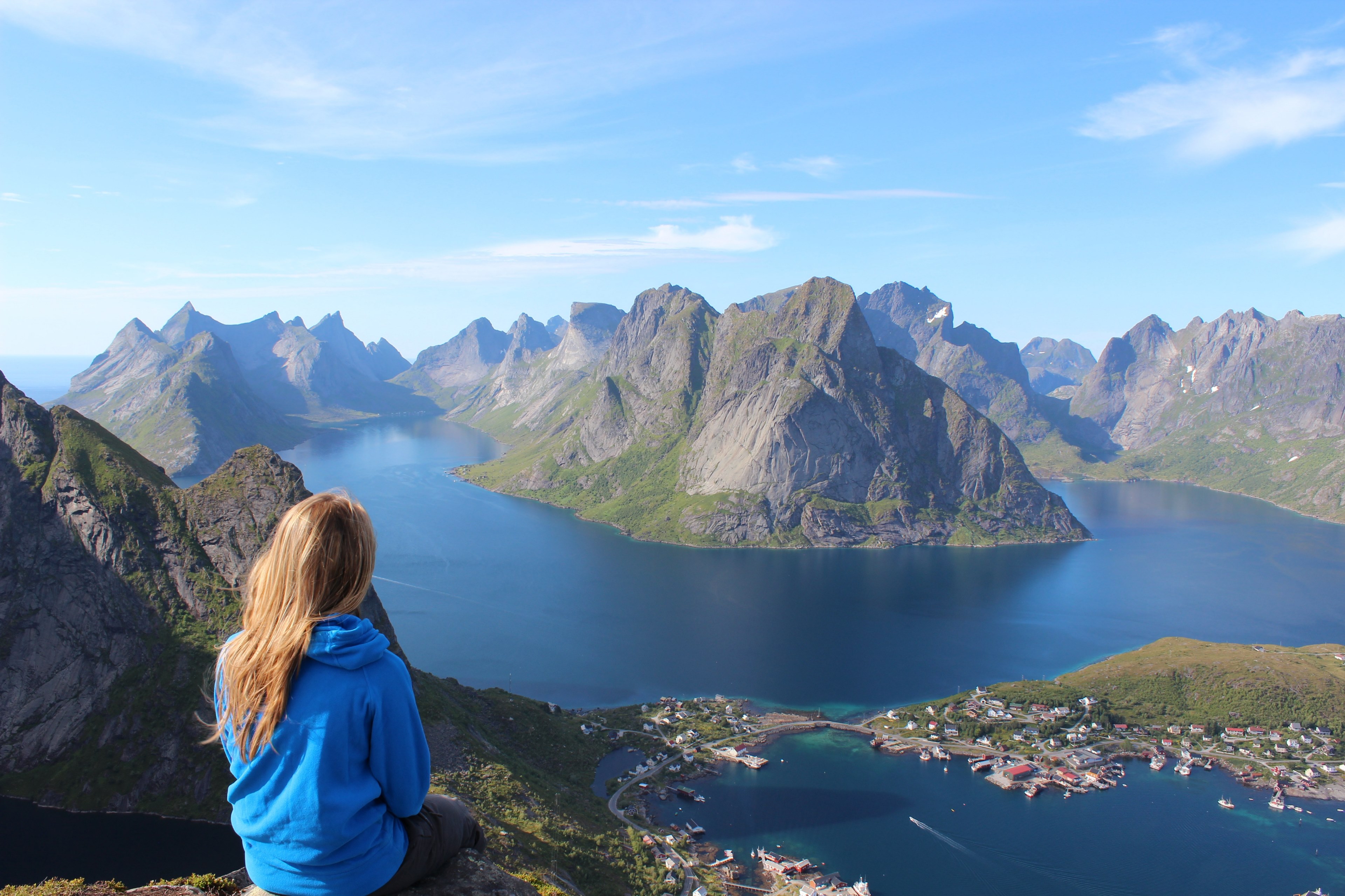 a blonde woman in a hoodie sitting on a ledge over a town on a mountain lake, scenic view of a town on a lake 4k, HD Wallpaper