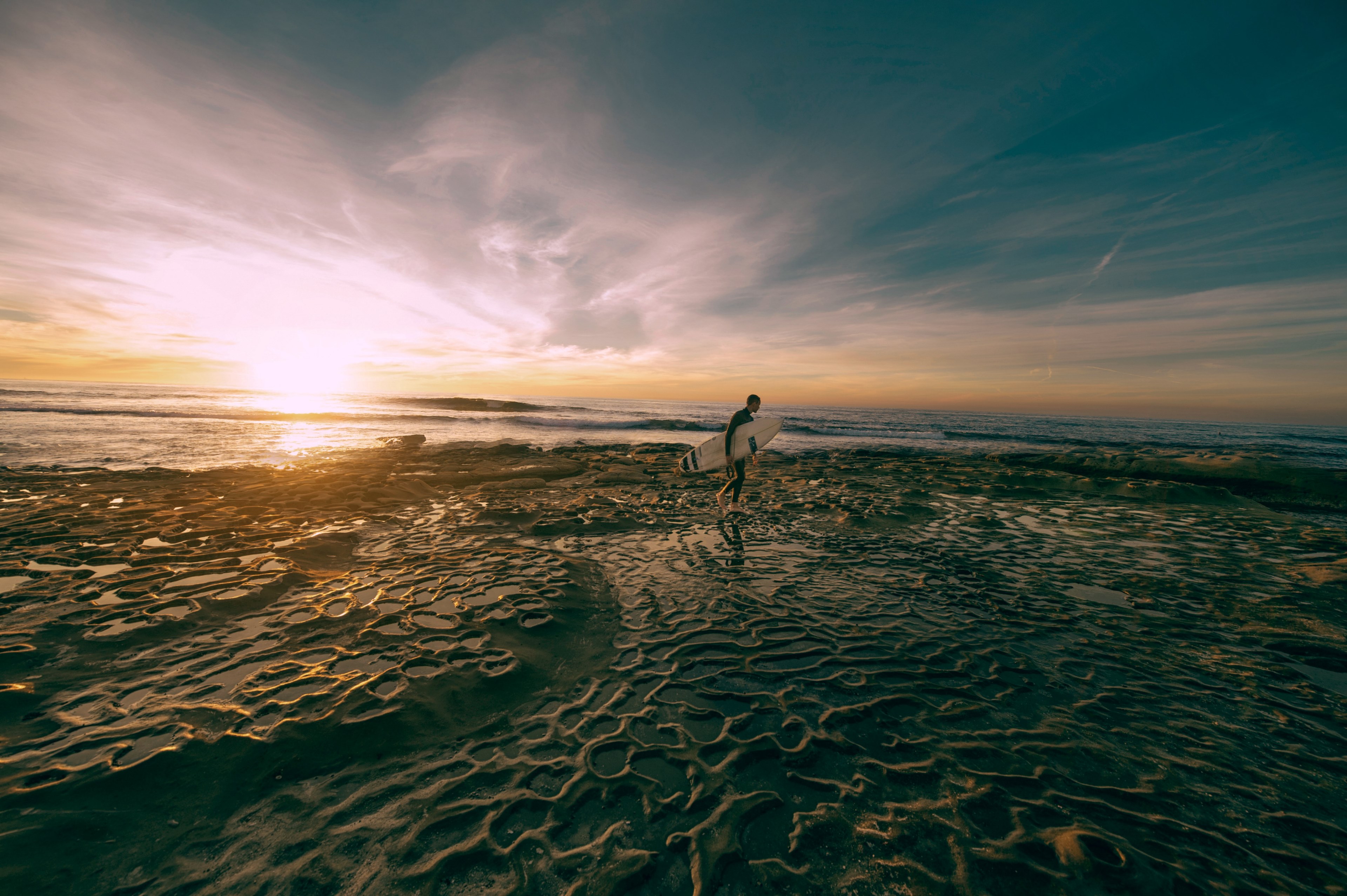 a man carries a surfboard across wet wavy sand beach during low tide as sun sets on the horizon, sunset sunrise dusk and dawn 4k, HD Wallpaper