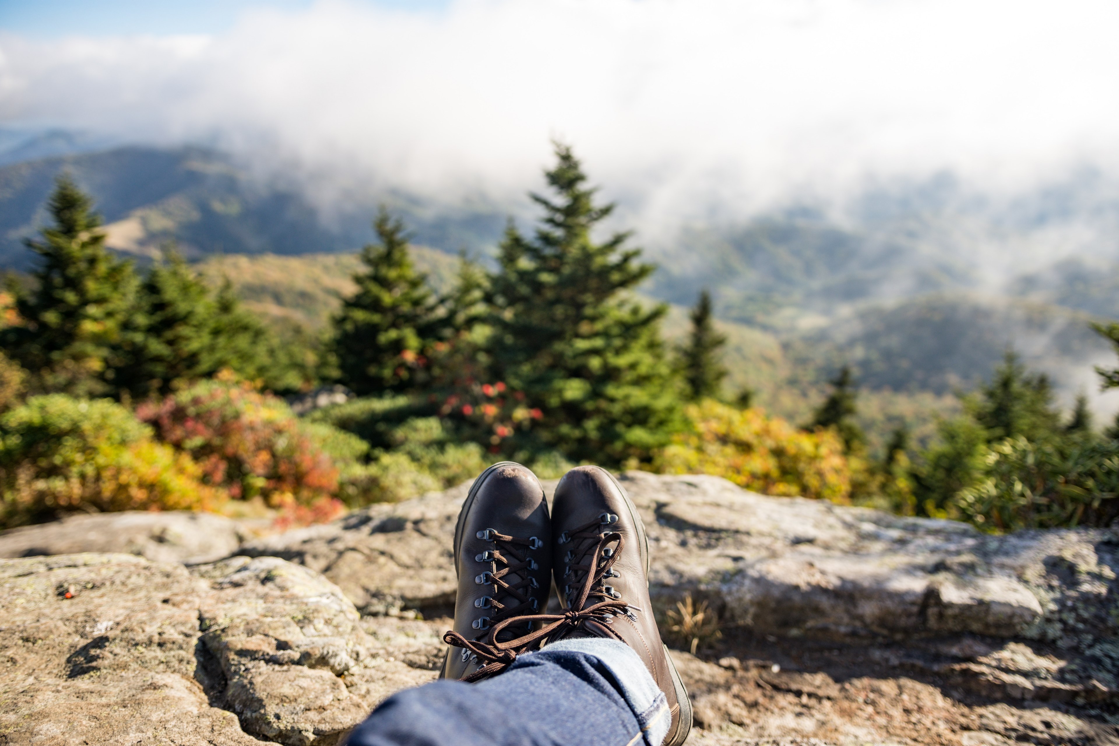 a person wearing hiking boots and jeans resting on a rock looking out into the fog covered mountains, resting over a valley 4k, HD Wallpaper