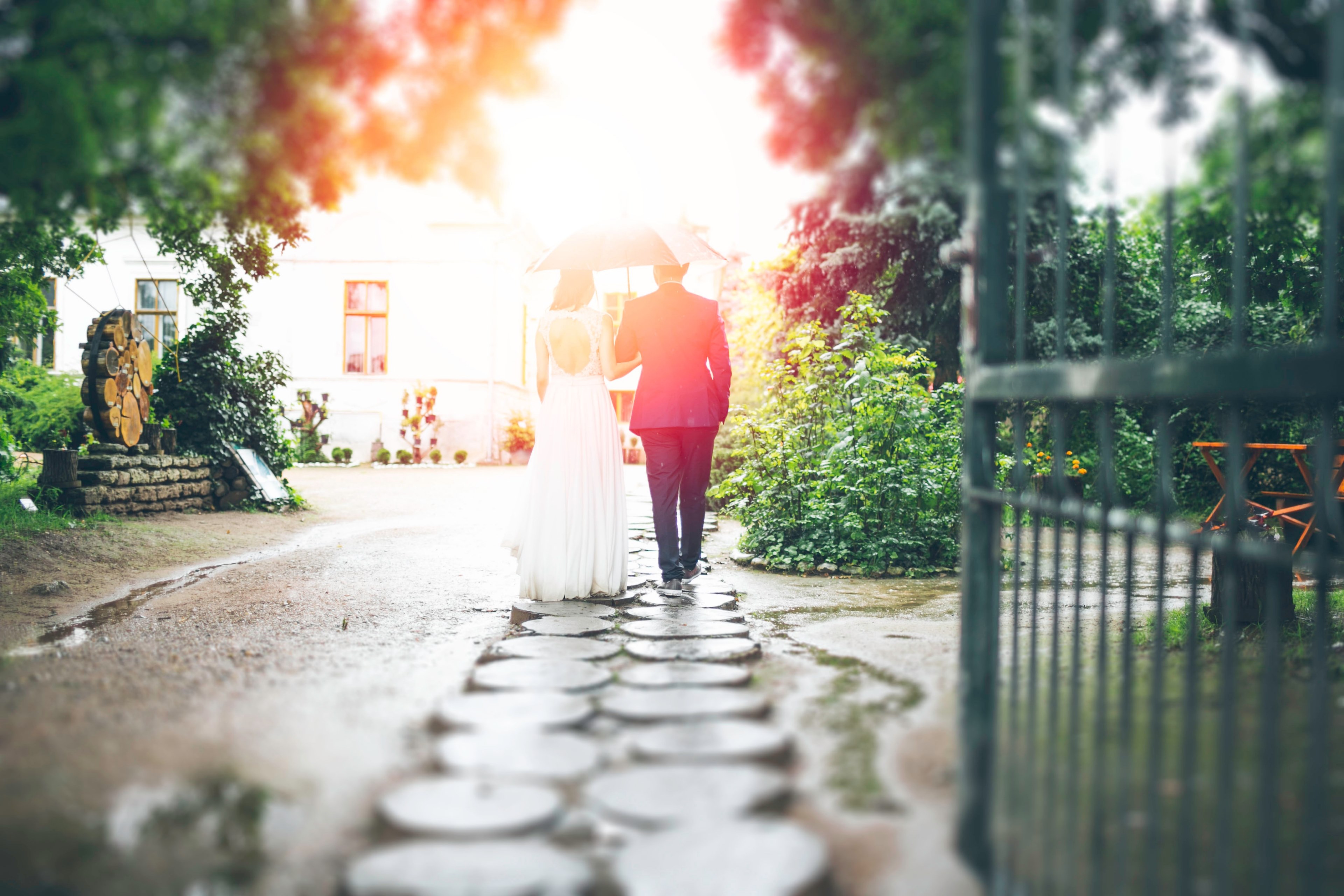 bride and groom walking down a stone path holding an umbrella with light shining on them, newlyweds walking down stone walkway 4k, HD Wallpaper