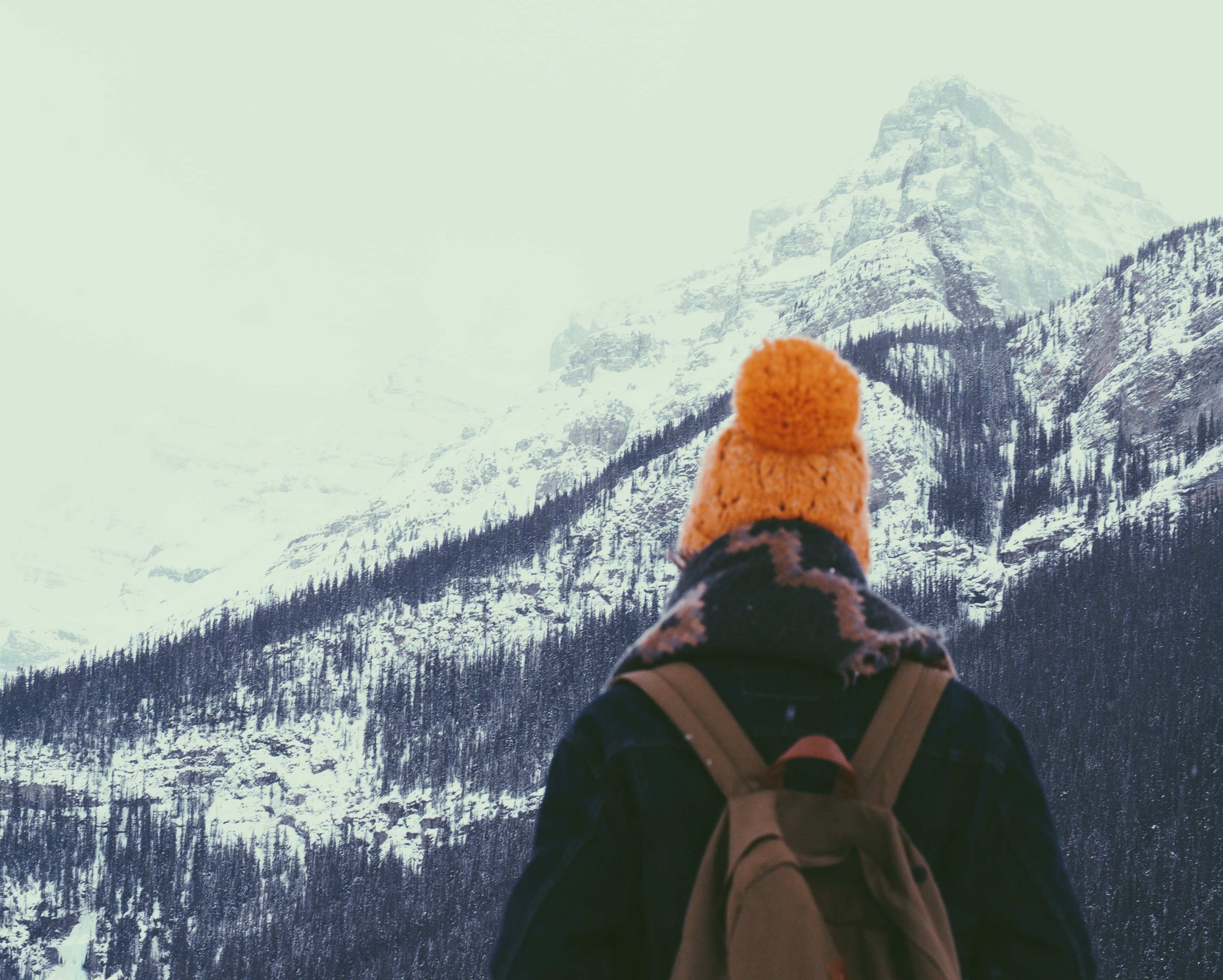 a person wearing a knit hat big scarf denim jacket and brown backpack looking out at lake louise on a snowy winter day, hiking on a snowy mountain 4k, HD Wallpaper
