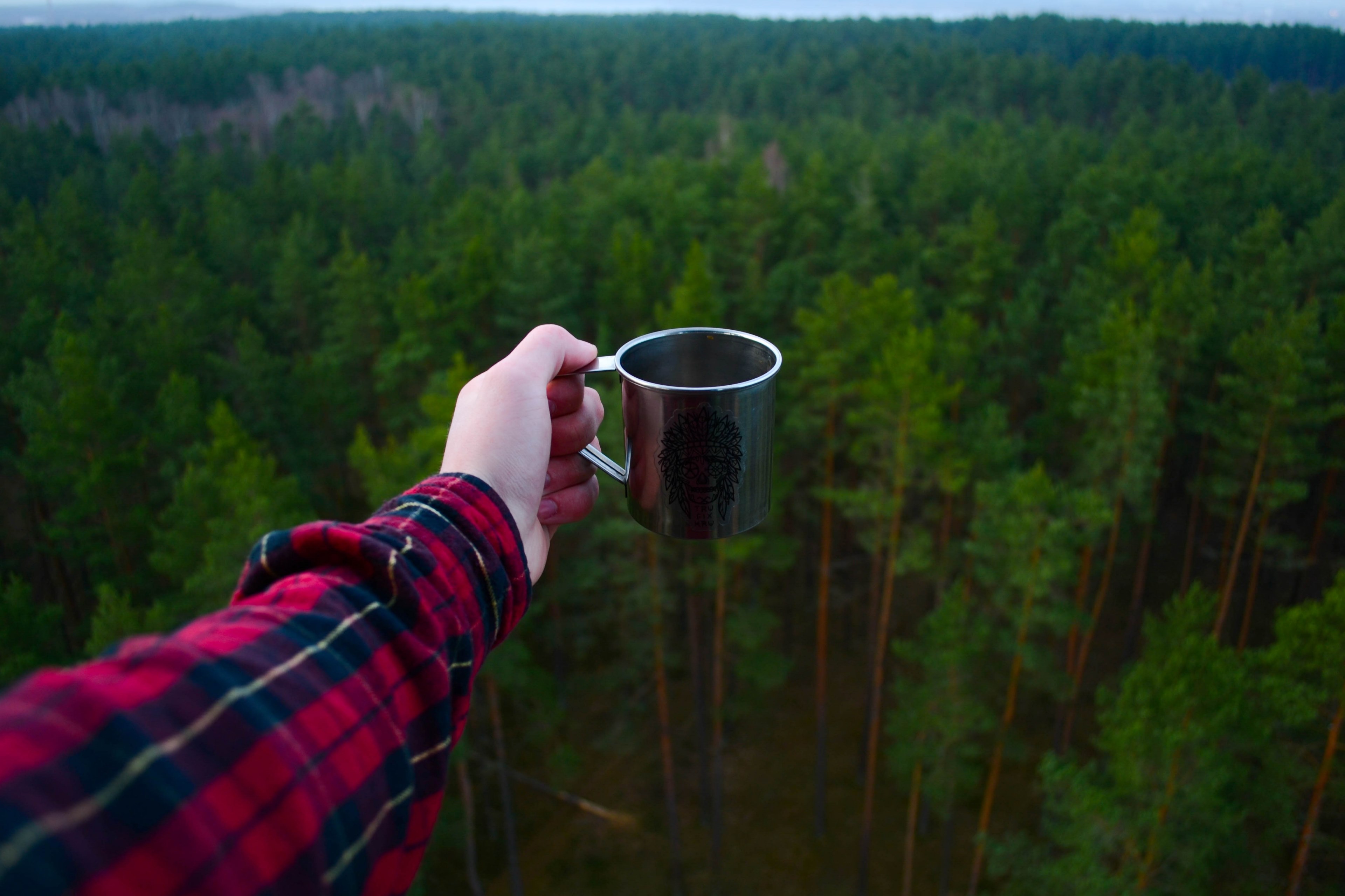 an outstretched arm of a person in a flannel shirt holding a mug with a view on a green forest, steel mug over a forest 4k, HD Wallpaper