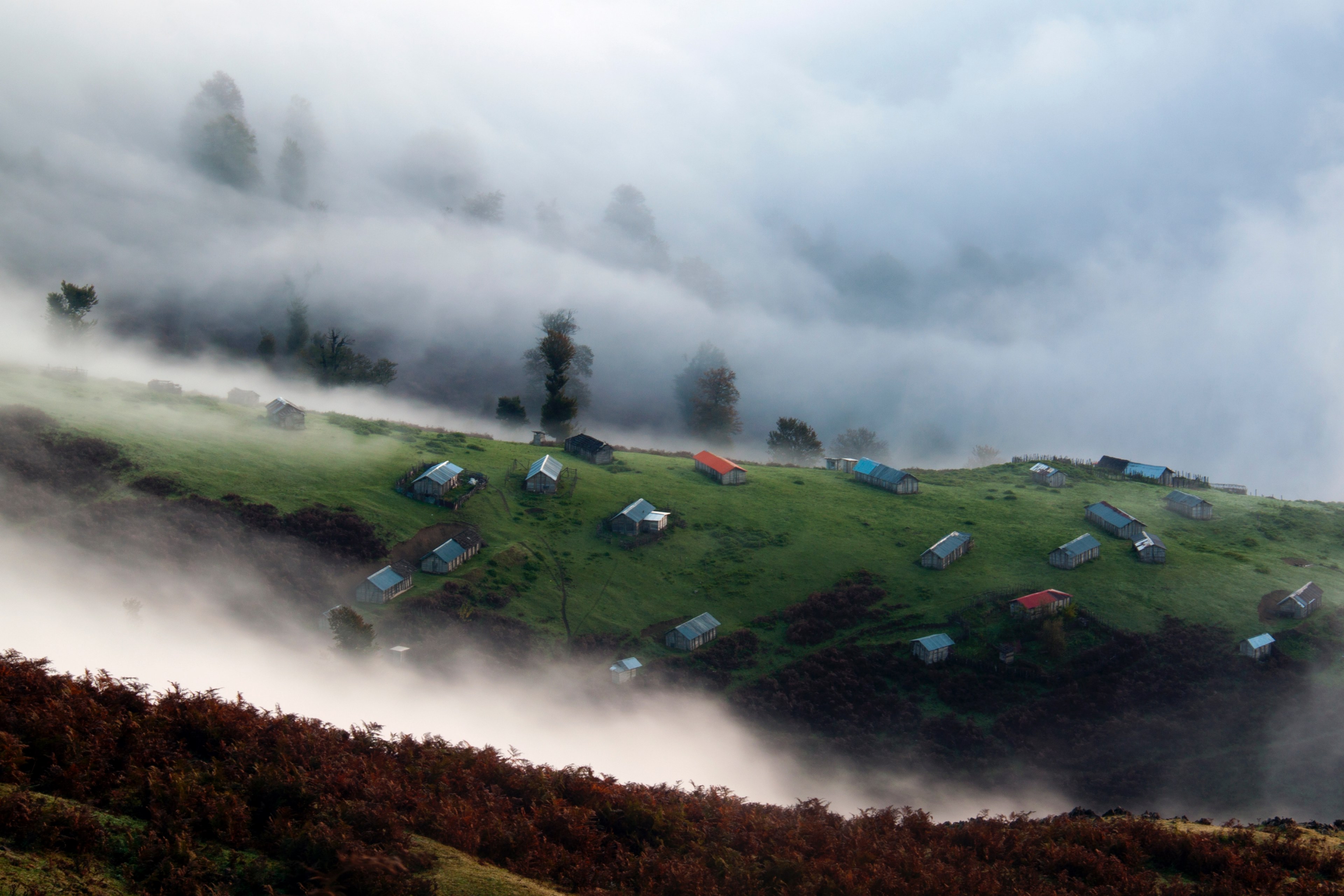 aerial view of multiple houses on a grassy hill with other hills and clouds surrounding them, buildings on a green slope 4k, HD Wallpaper