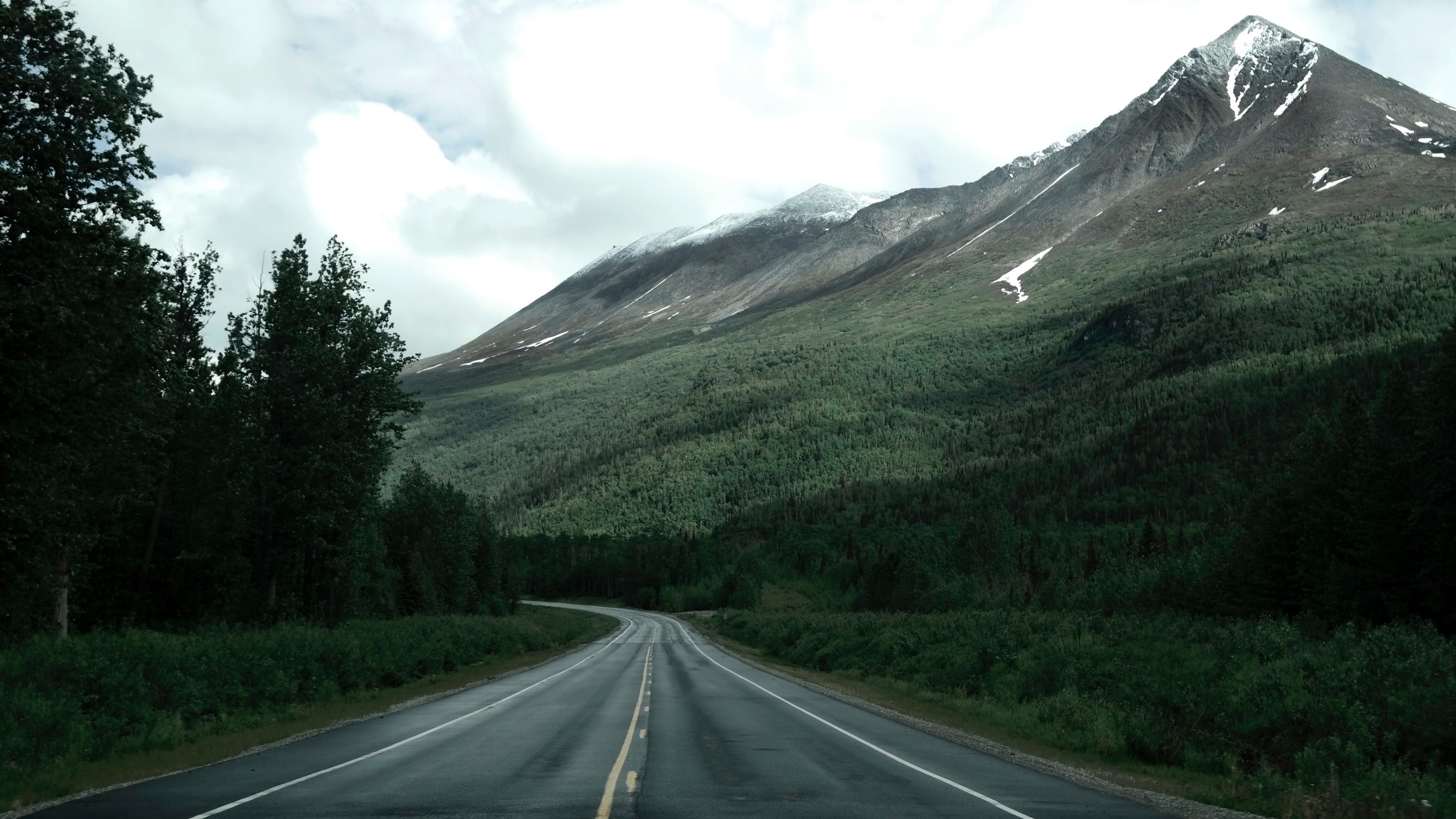 an empty asphalt road near a wooded slope of tall snow capped mountains, road along alaska mountains 4k, HD Wallpaper