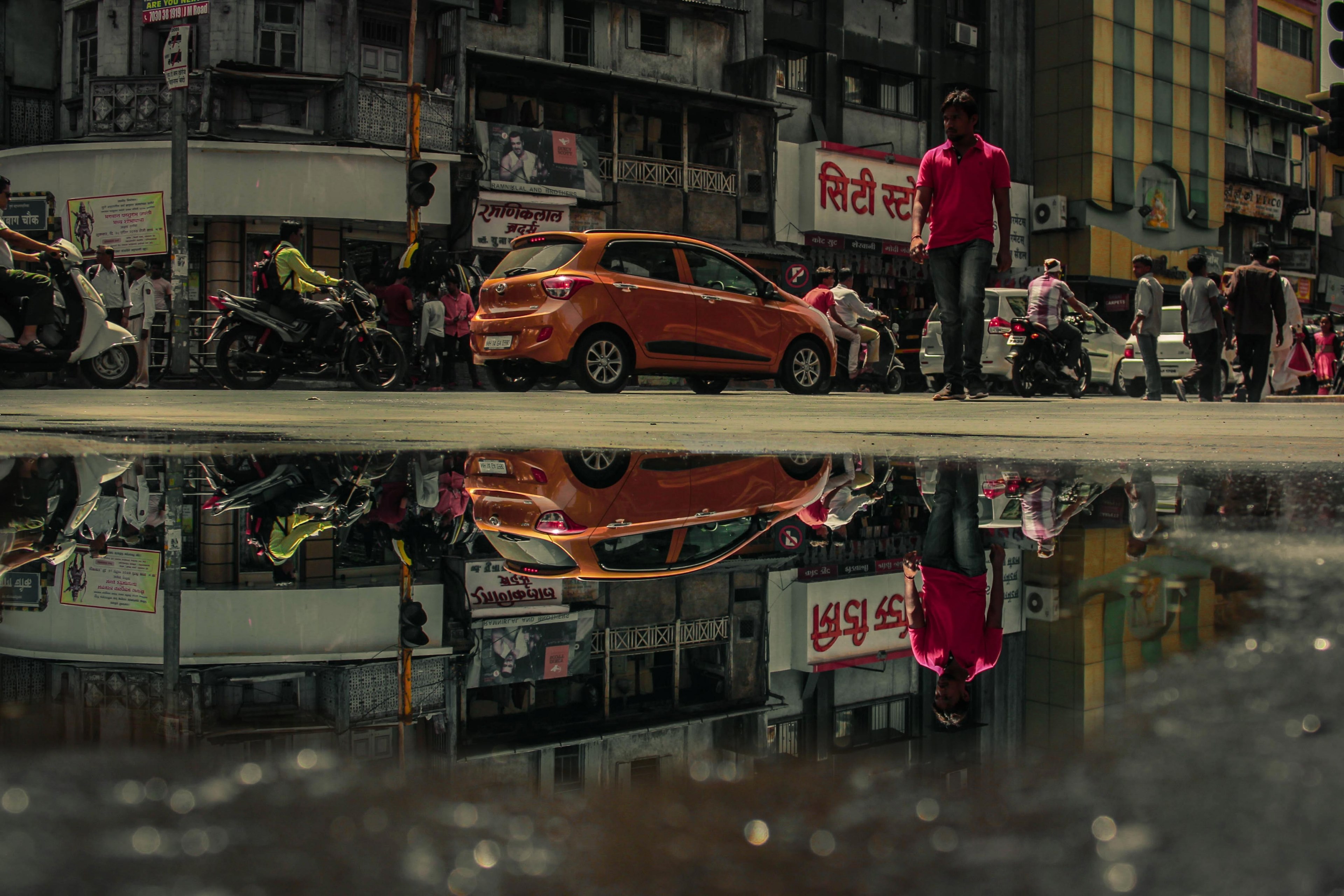 street puddle reflection of the man in pink polo shirt small orange car and several motorcycles in pune, parallel worlds 4k, HD Wallpaper
