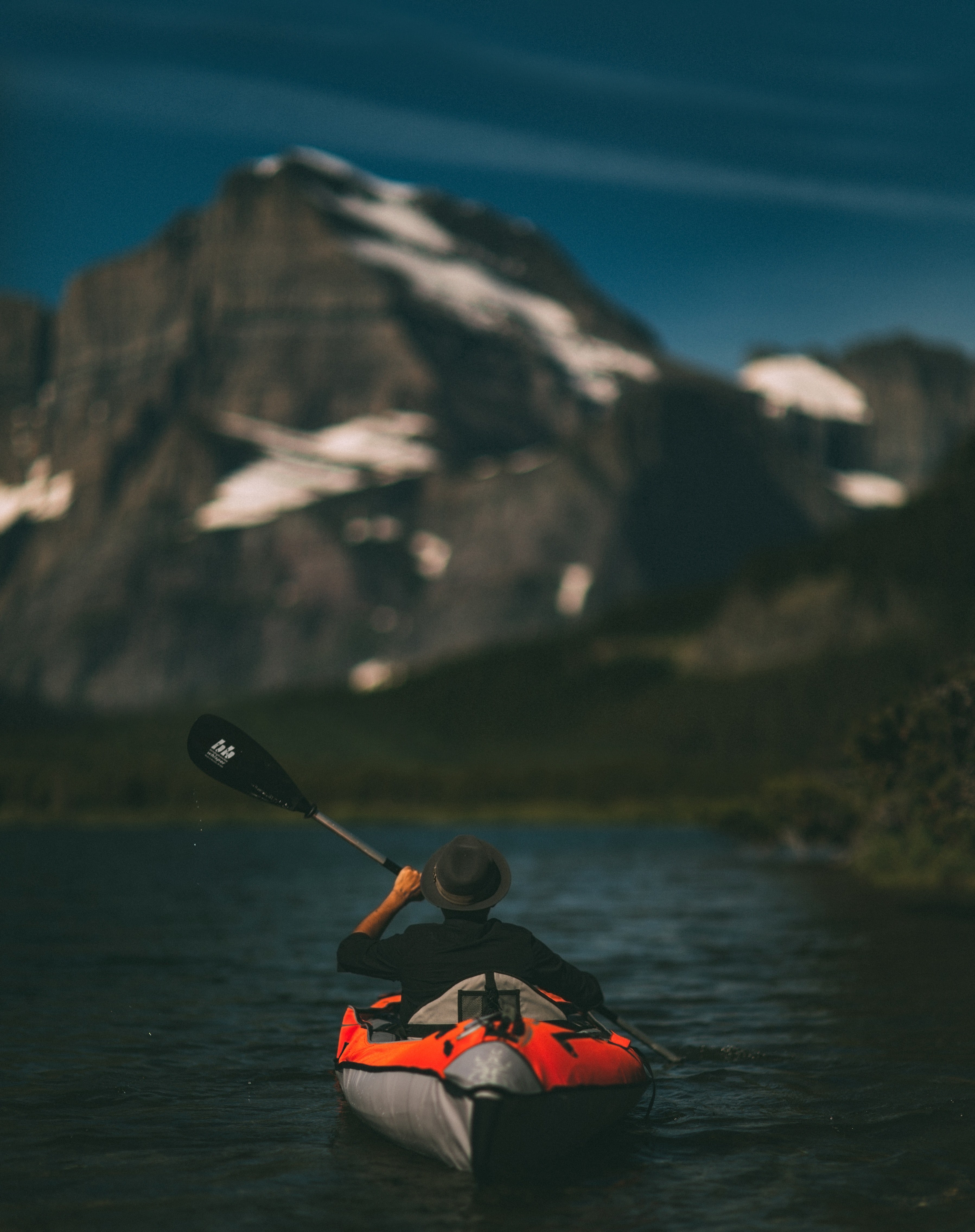 a man wearing a hat paddling in a blow up orange canoe in swiftcurrent lake, swiftcurrent lake canoe 4k, Phone HD Wallpaper