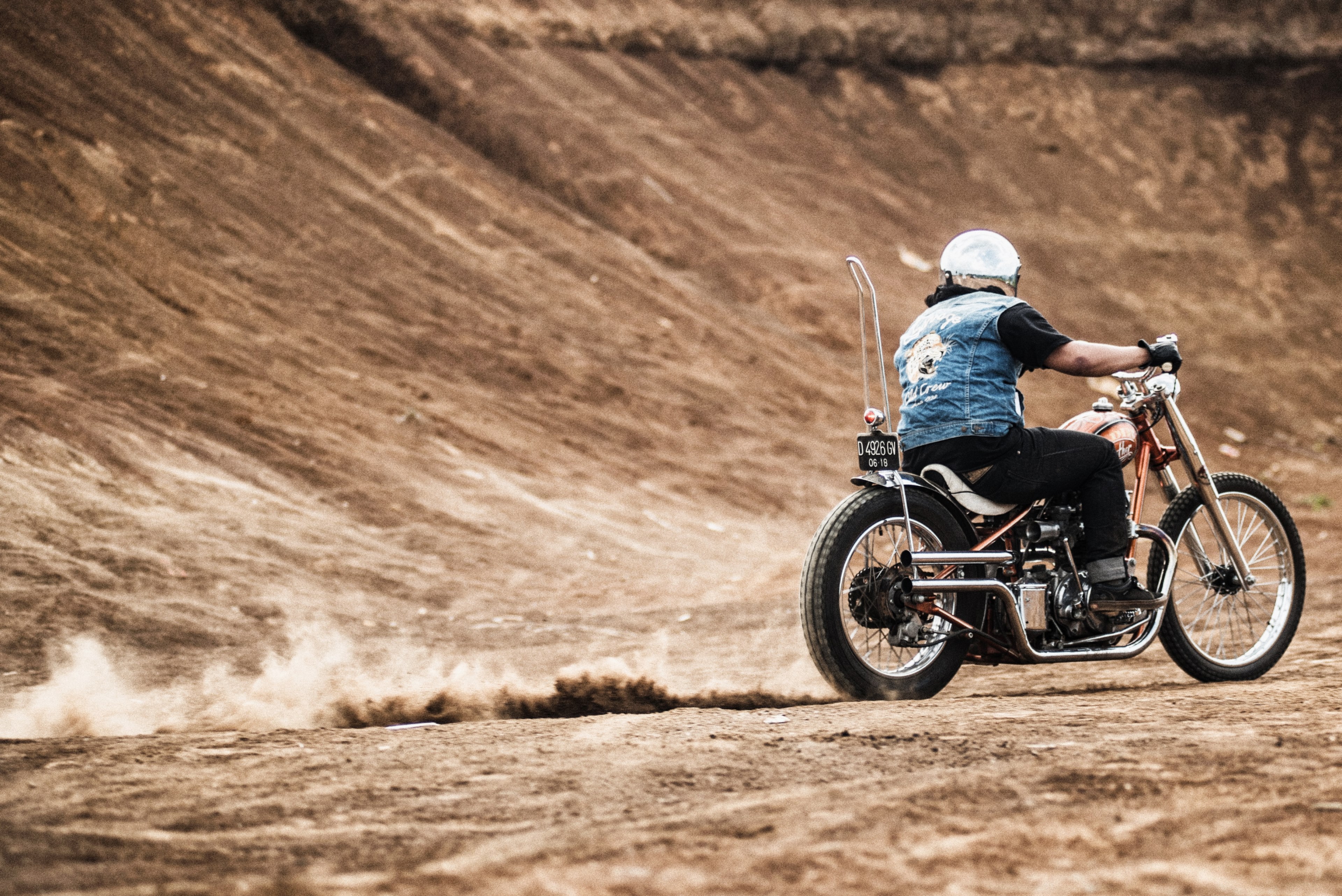 a motorcyclist in a denim jacket and reflective helmet riding his bike and leaving a trail of dust by a dirt mound, motorcyclist revving bike 4k, HD Wallpaper