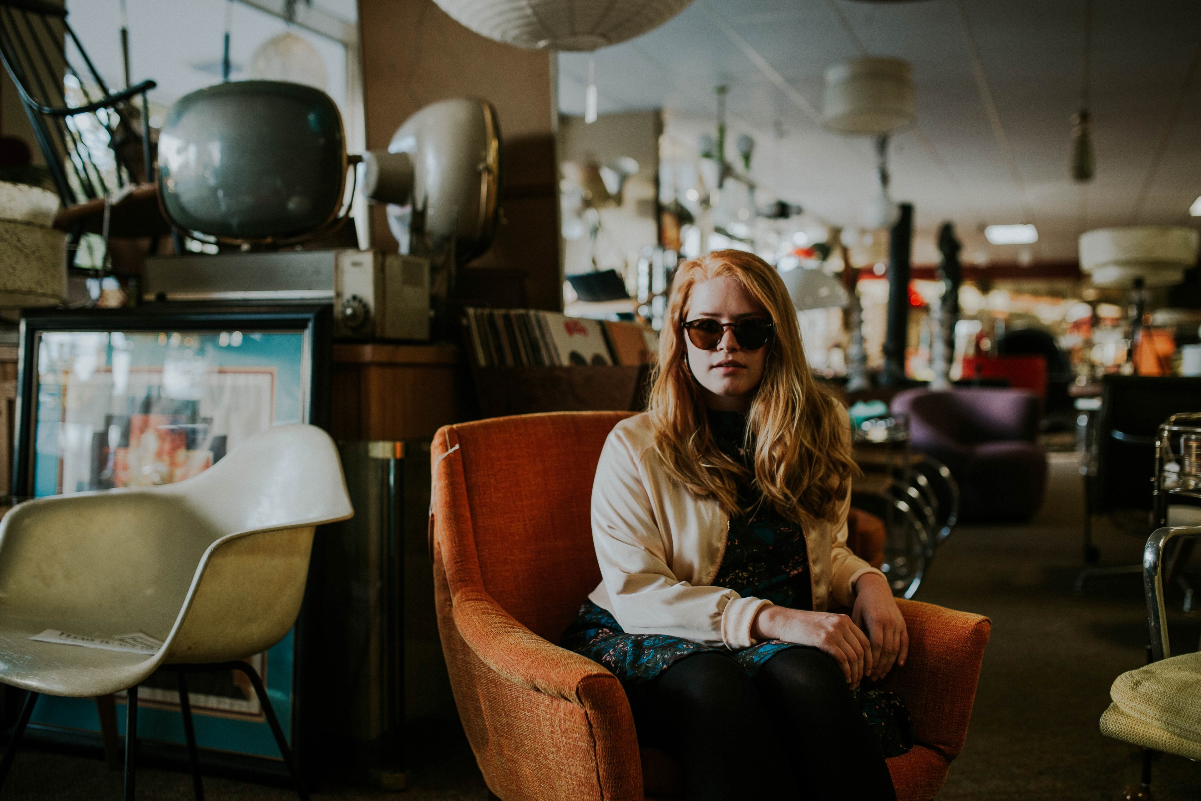 a woman in sunglasses sits on an orange chair inside a secondhand store, cic 4k, HD Wallpaper