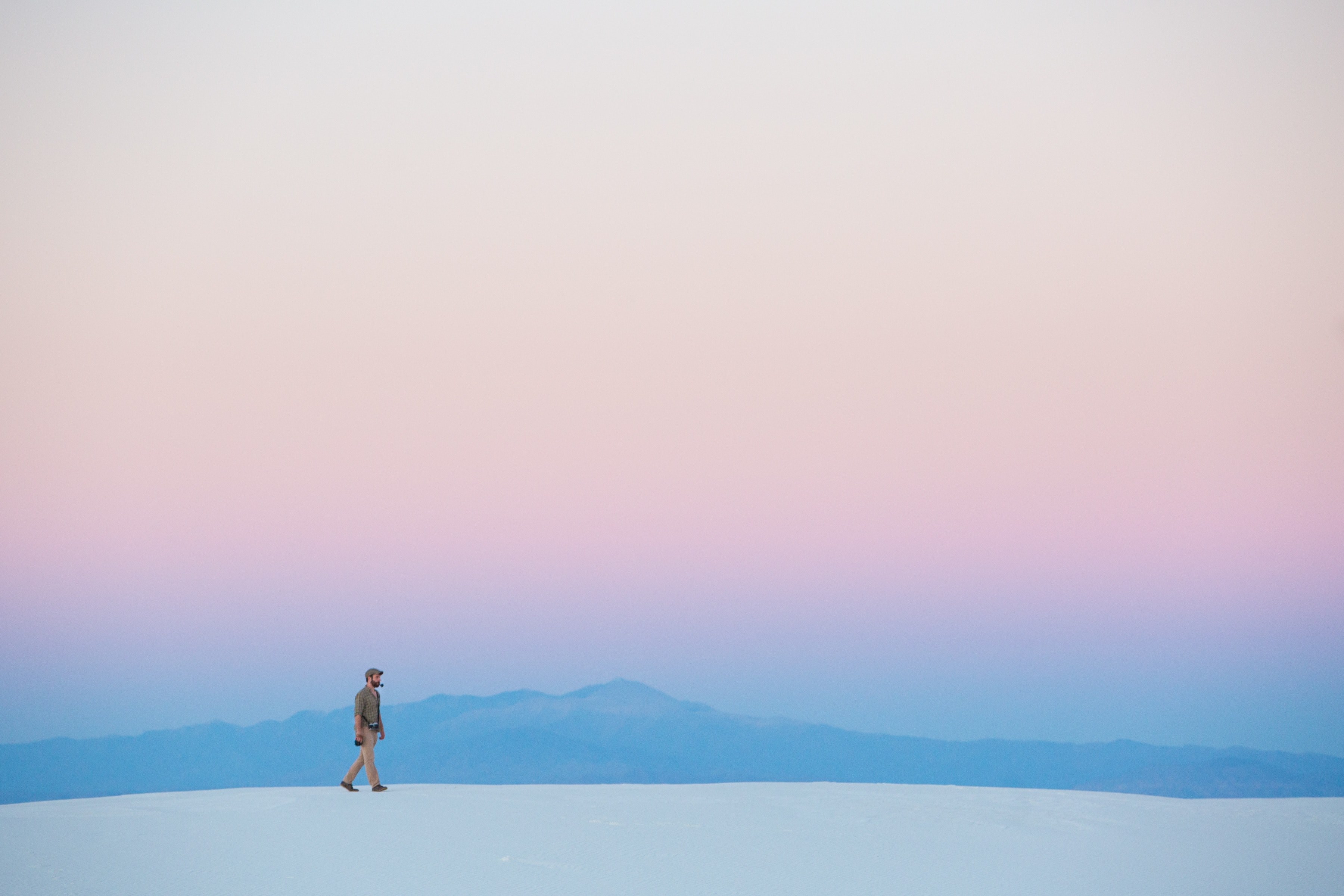 a dreamy shot of a man walking along a white sand dune with a mountain range on the horizon, minimal hike on the dunes 4k, HD Wallpaper
