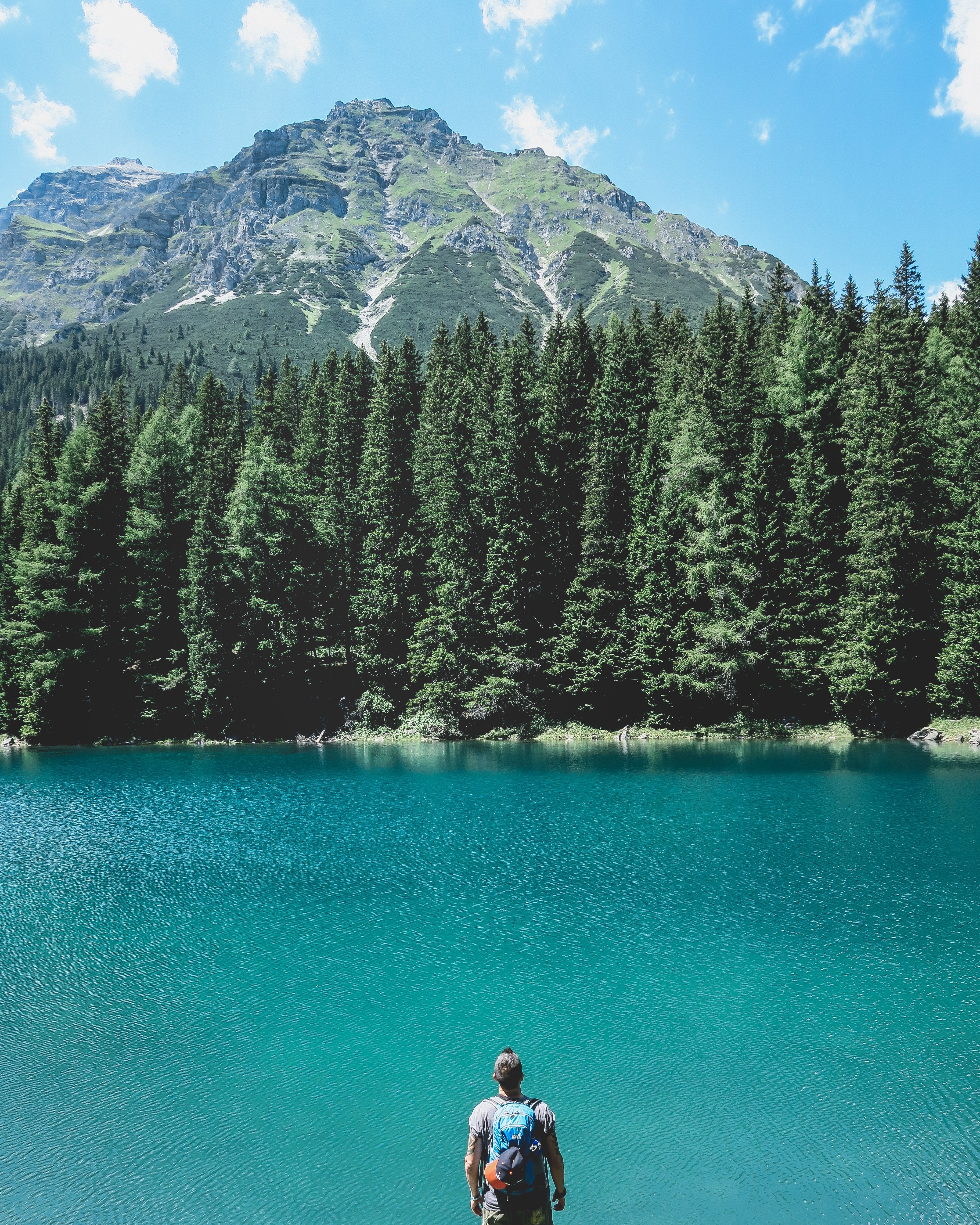 a male backpacker looking at a tall mountain across a blue lake, hiker over a mountain lake 4k, Phone HD Wallpaper