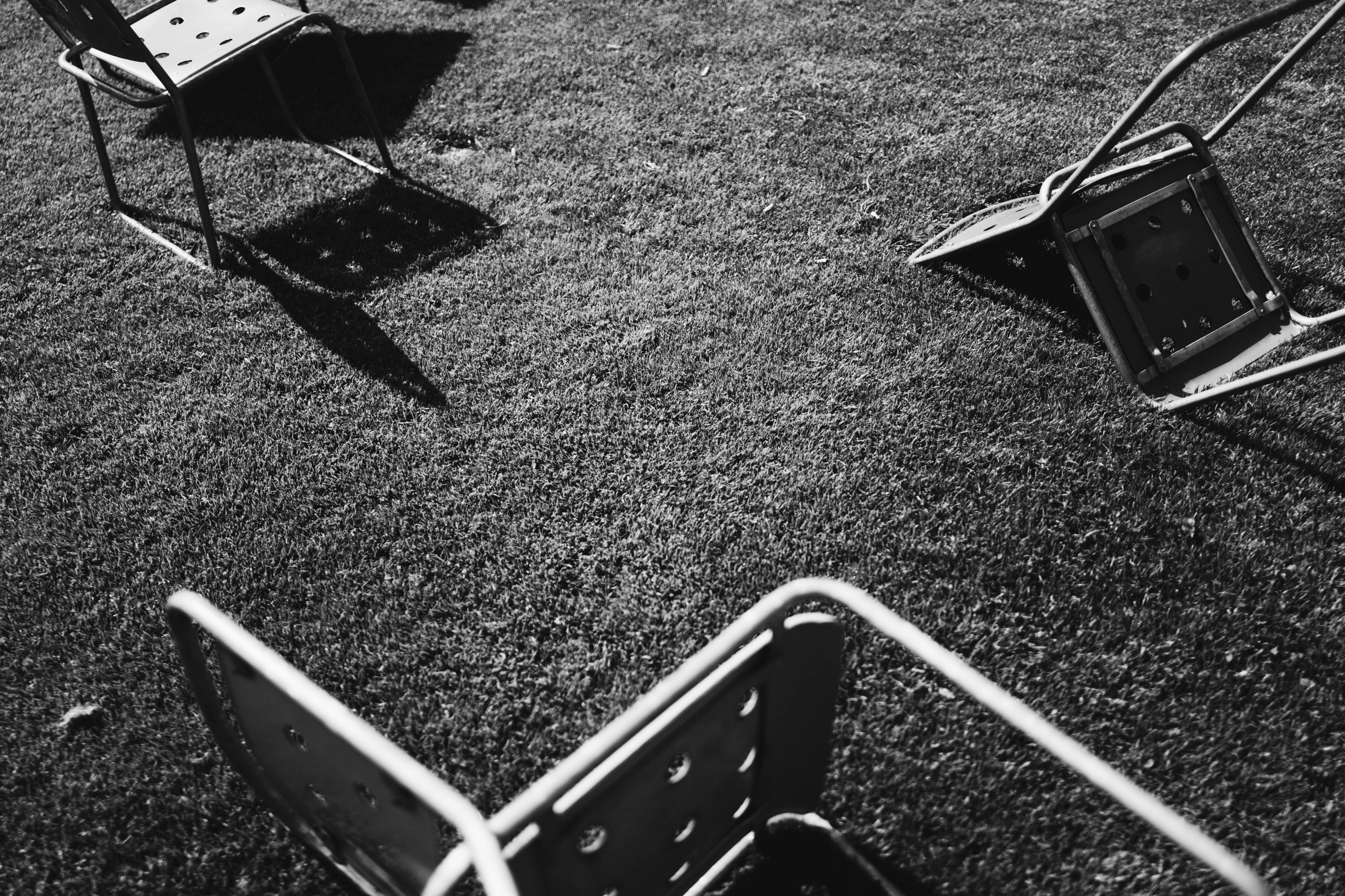 black and white photo of fallen chairs on grass with shadow, fallen chairs on grass 4k, HD Wallpaper