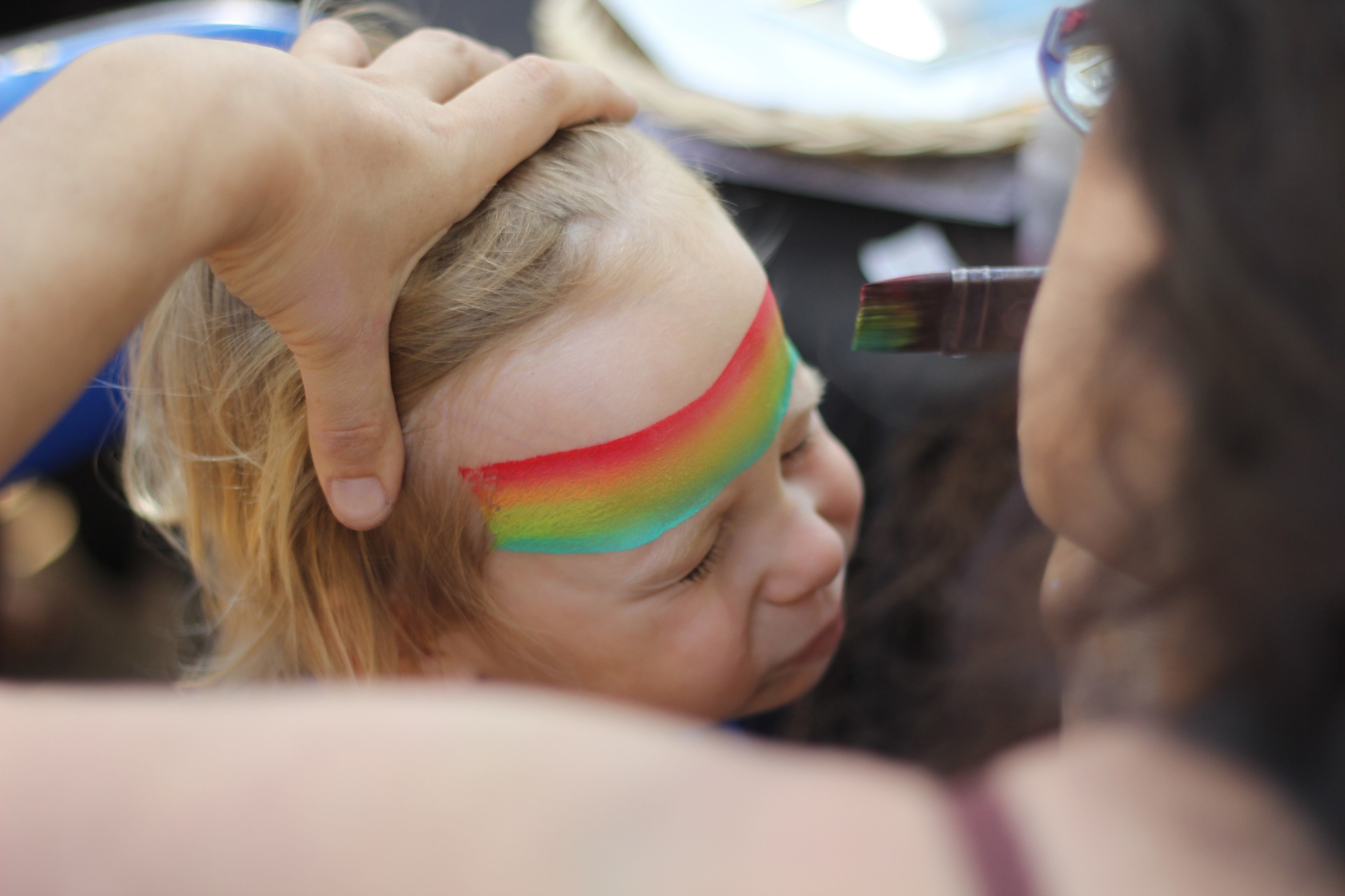 a woman painting a tri color stripe on a childs forehead, rainbow on a childs forehead 4k, HD Wallpaper