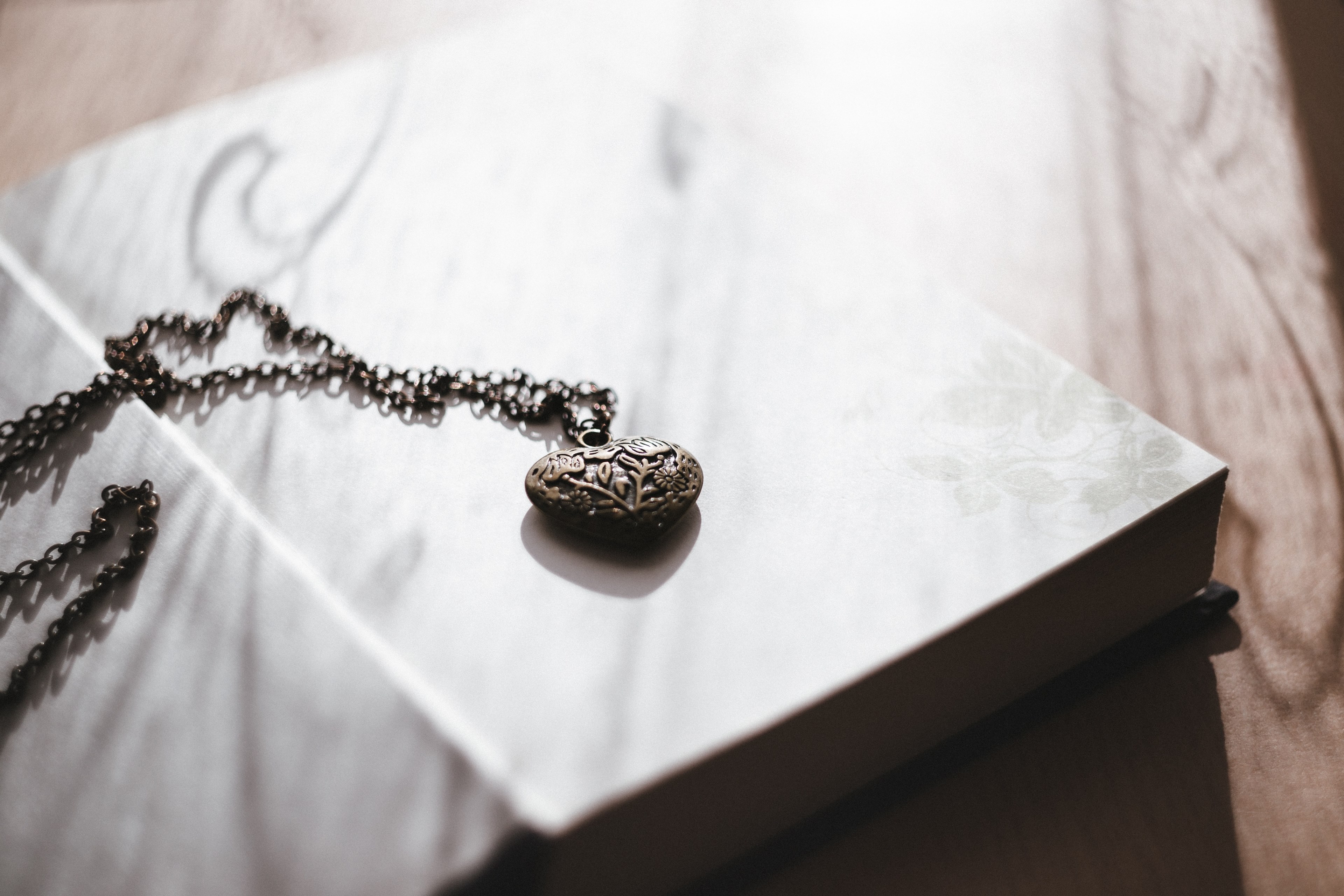 sun falls on an antique locket which sits atop an open book, locket on open book 4k, HD Wallpaper