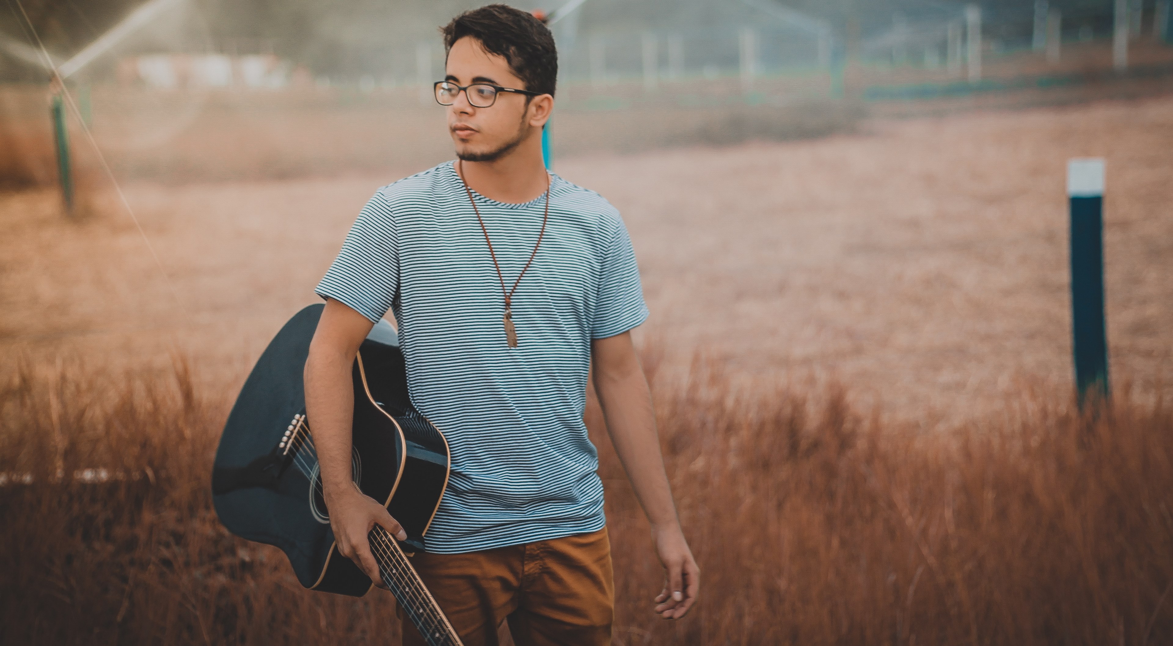 a man in a striped shirt with glasses is holding a guitar in a field, _man holding a guitar 4k, HD Wallpaper