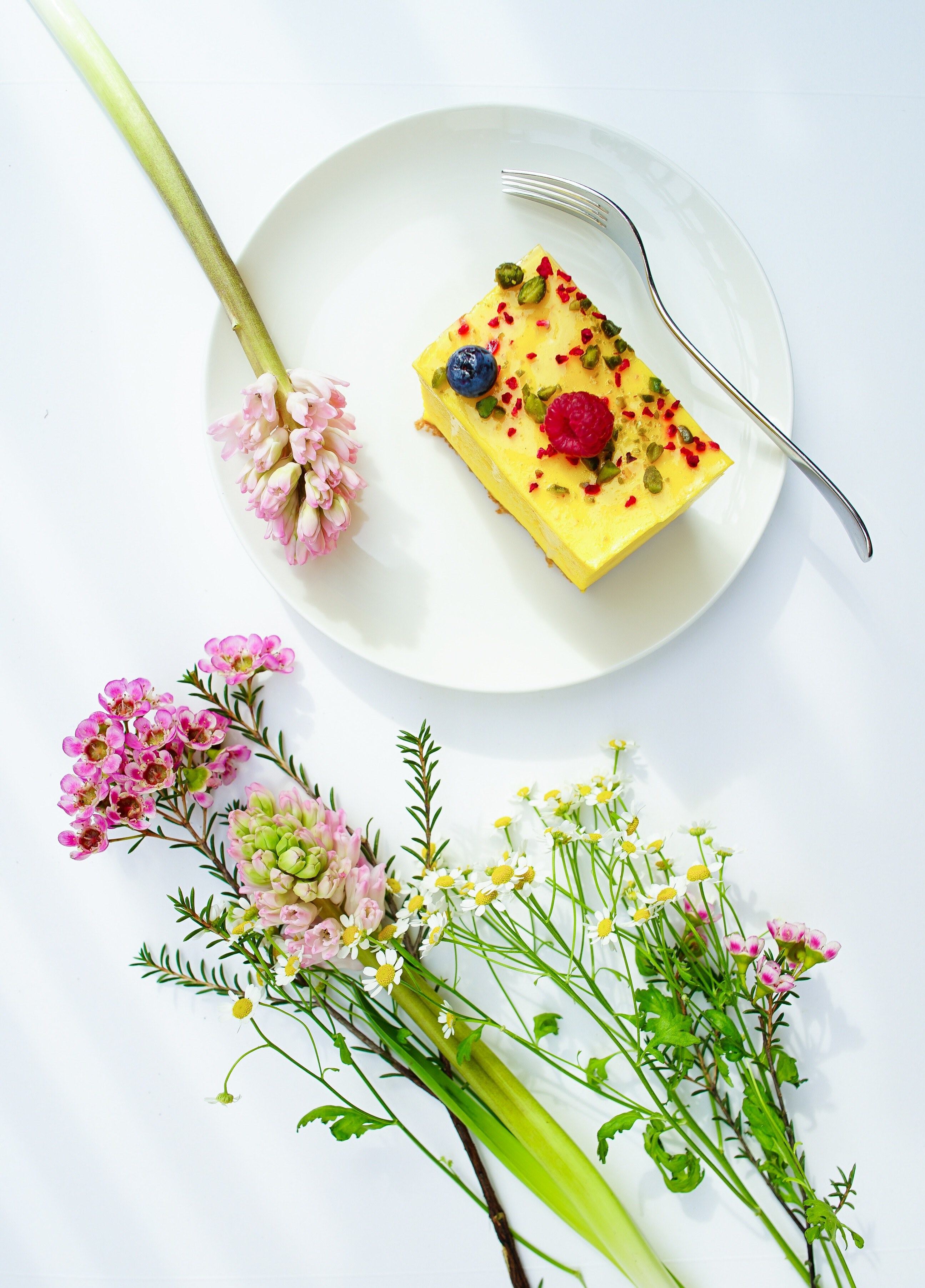 an overhead shot of a piece of cheesecake on a plate next to small bouquets of various flowers, saffron cheesecake 4k, Phone HD Wallpaper