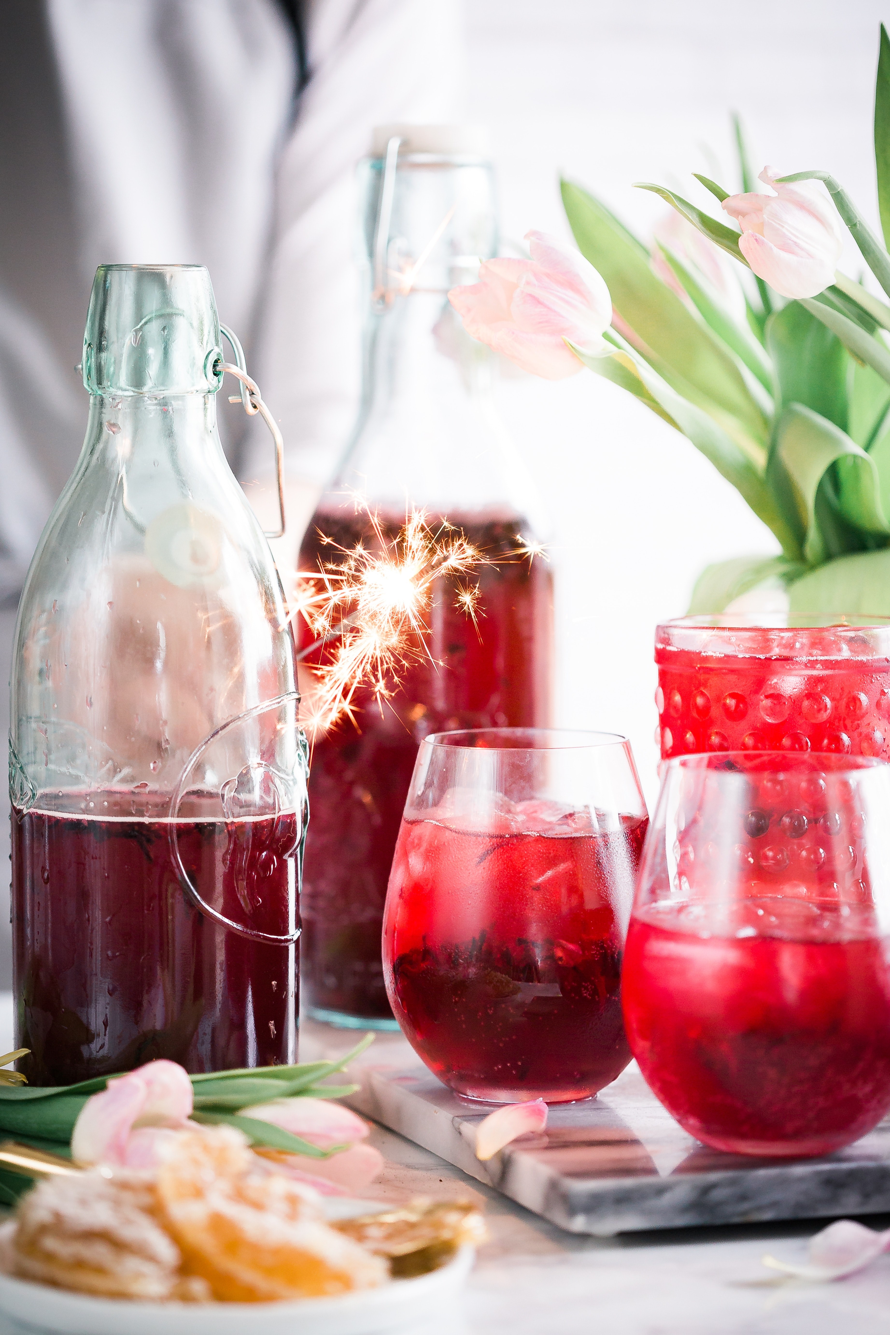 bottles and glasses with a red beverage next to flowers and a platter of citruses on a tabletop, spring party punch 4k, Phone HD Wallpaper