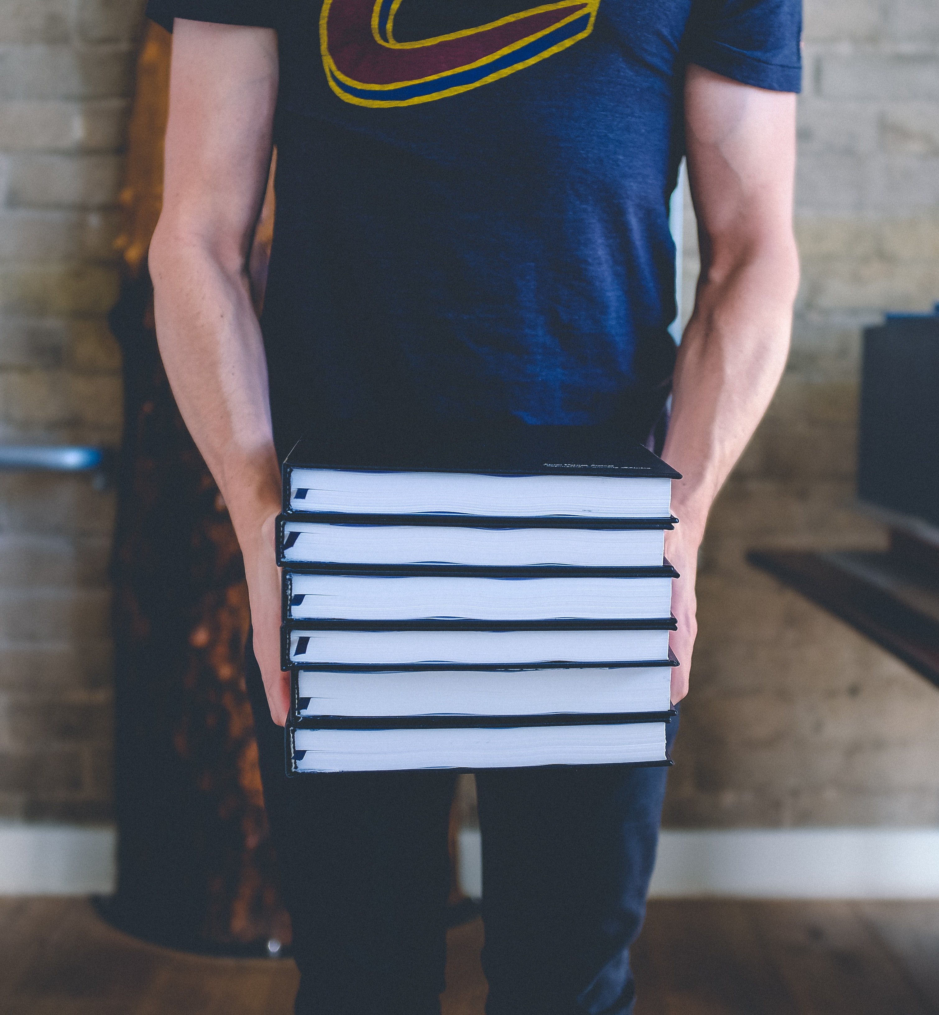 person in a t shirt carries a stack of books in front of an indoor brick wall, person with stack of books 4k, Phone HD Wallpaper