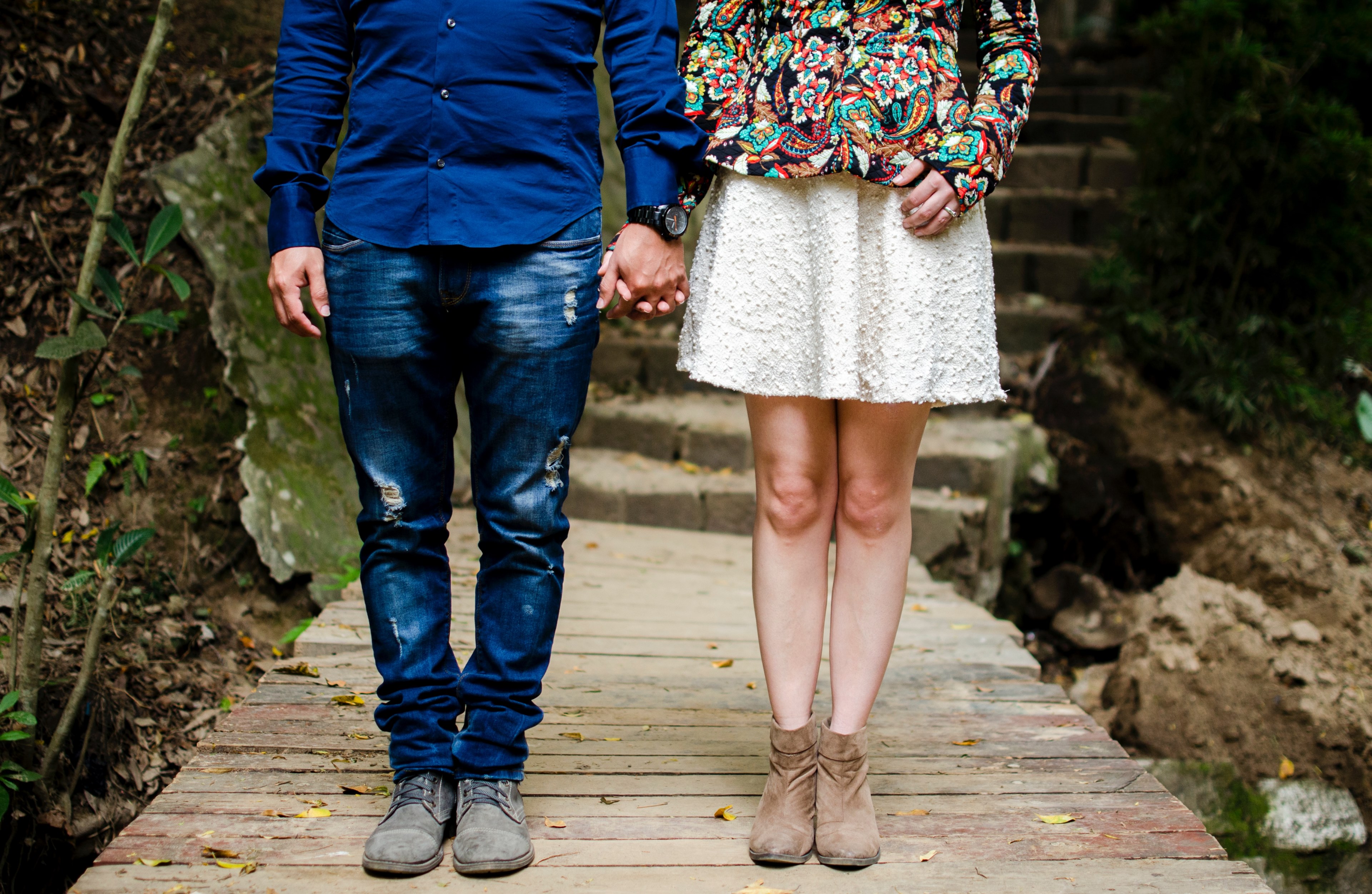 a couple in brightly colored clothes stands on a wood deck below stone stairs holding hands, holding hands on deck 4k, HD Wallpaper