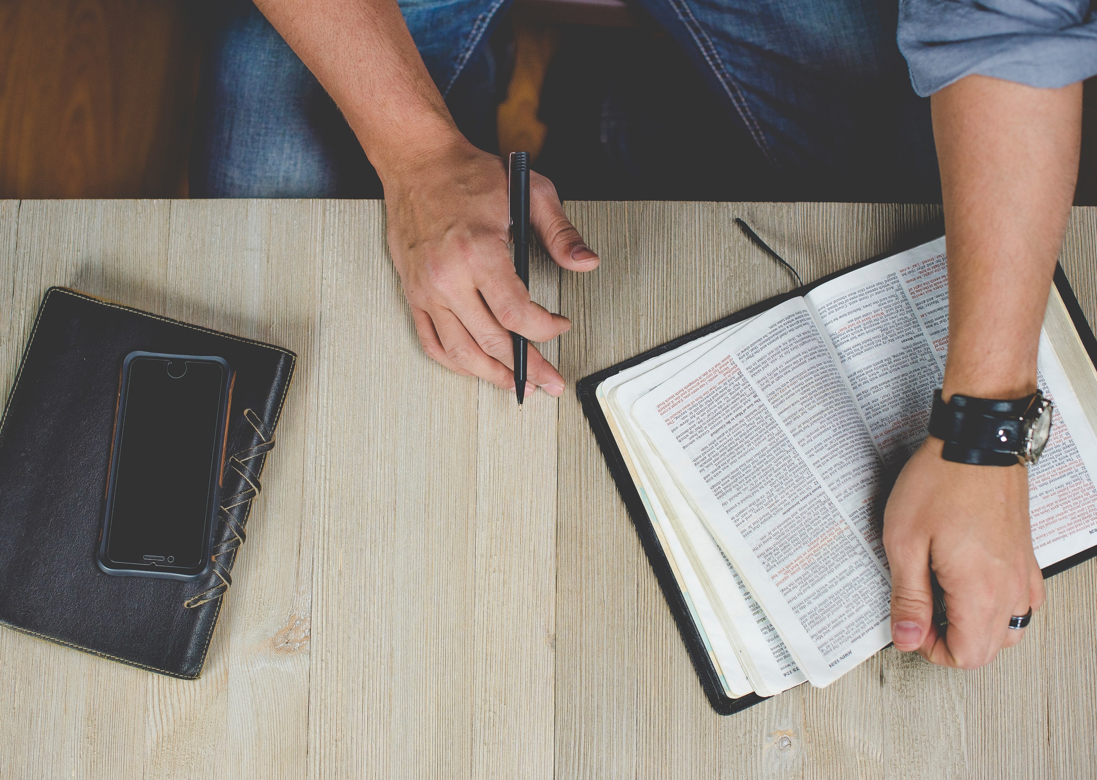 mans hands holding an open book and a pen on a wooden surface with a notebook and a phone, bible study 4k, HD Wallpaper