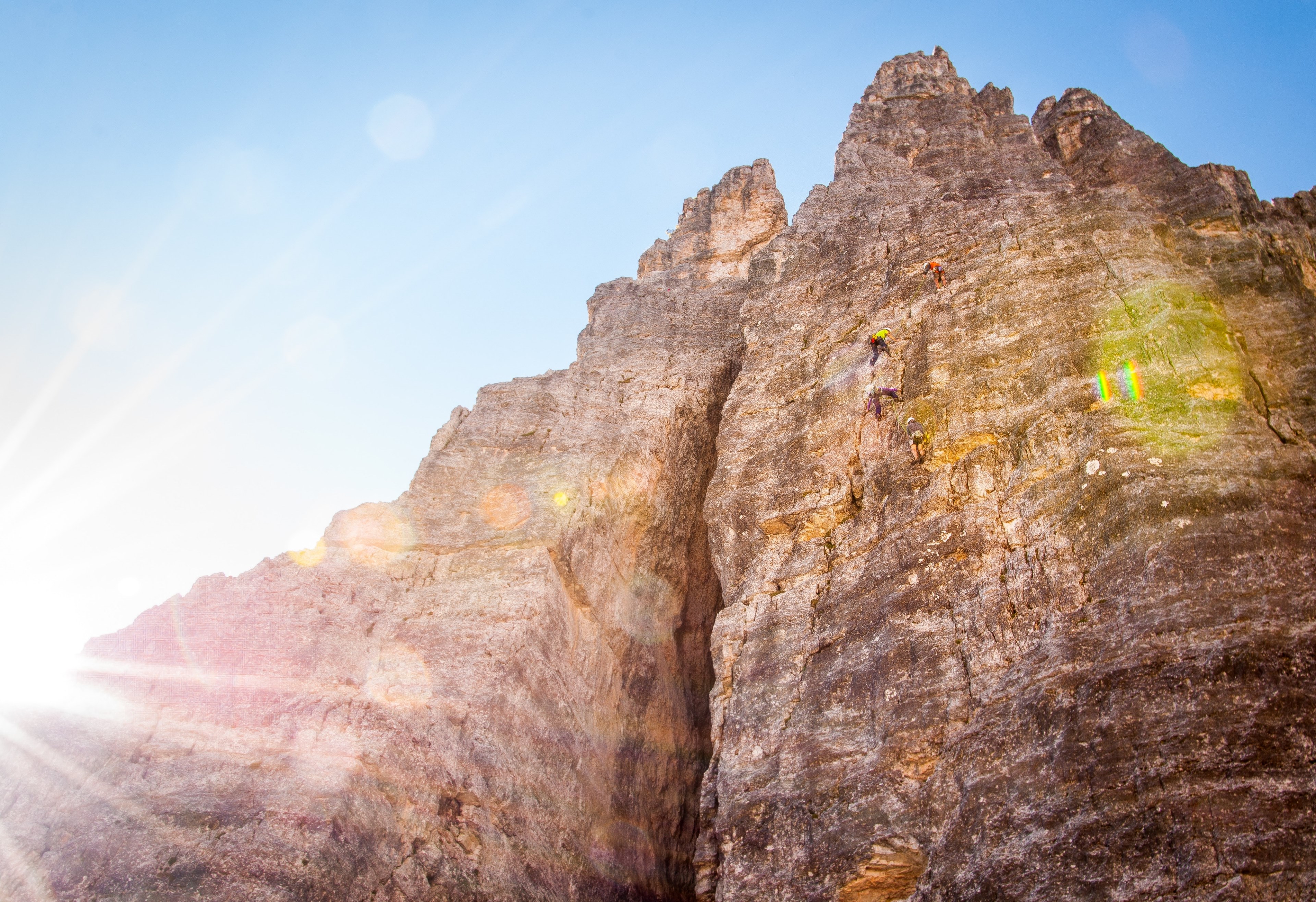 view from bottom of rocky cliffs with sun flare, mountaineers in action 4k, HD Wallpaper