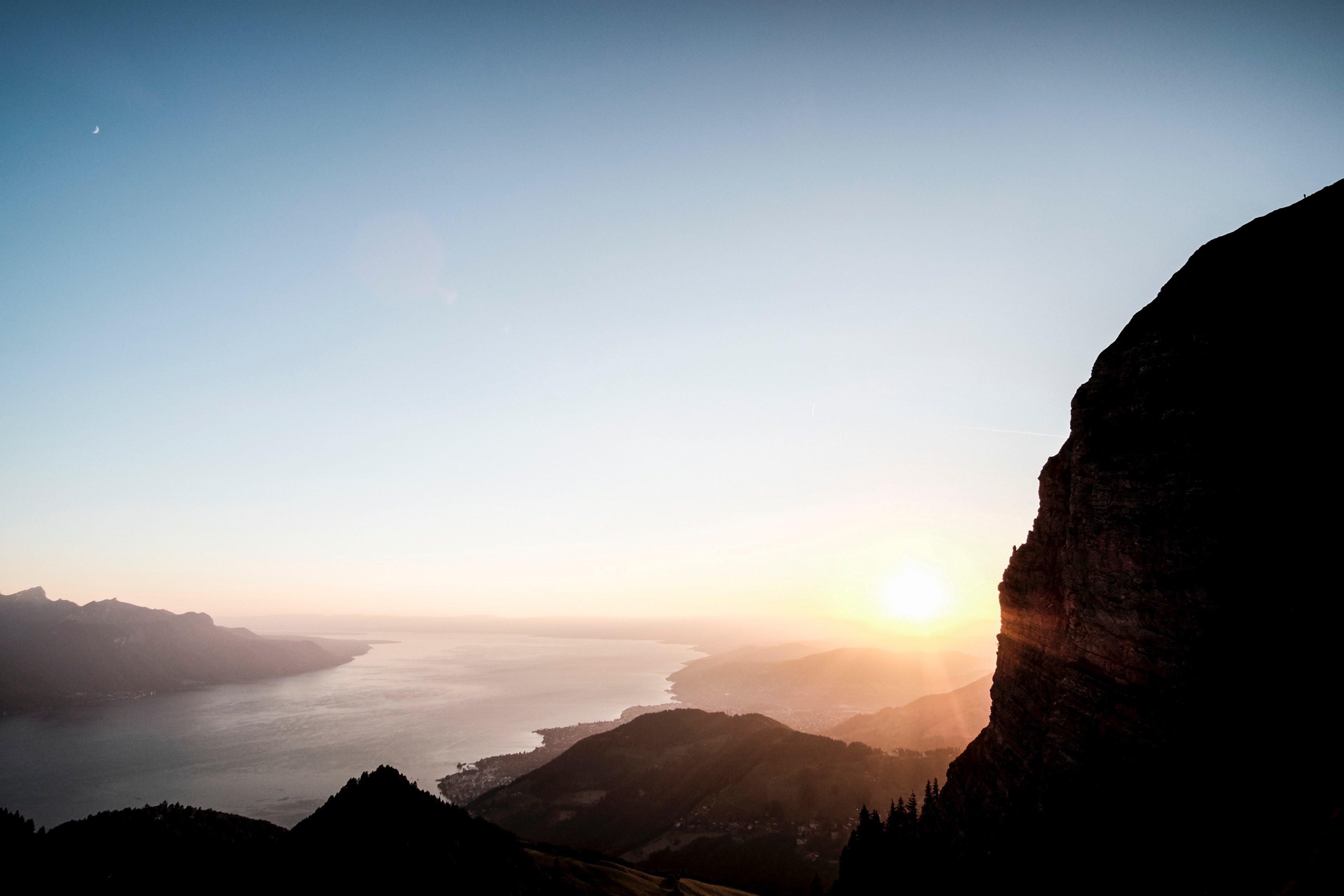 a view from the mountains at dent de jaman overlooking the water and surrounding hills towards a horizon of pale blue sky and yellow glaring sun, mountain sunset sunrise and dusk 4k, HD Wallpaper