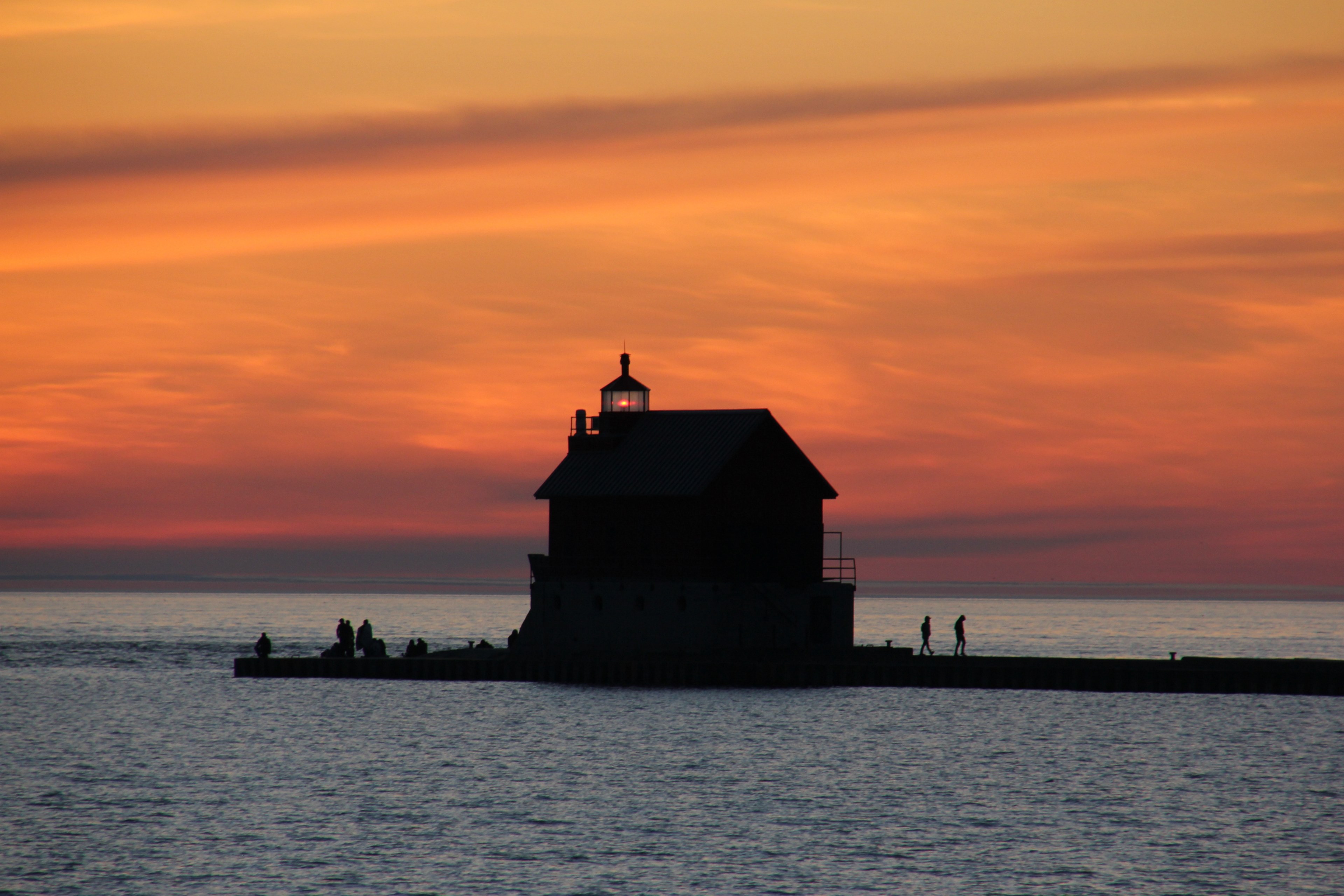 distant shot of a small lighthouse in the sea with people around a cloudy orange sunset above, sea dusk sunset and twilight 4k, HD Wallpaper
