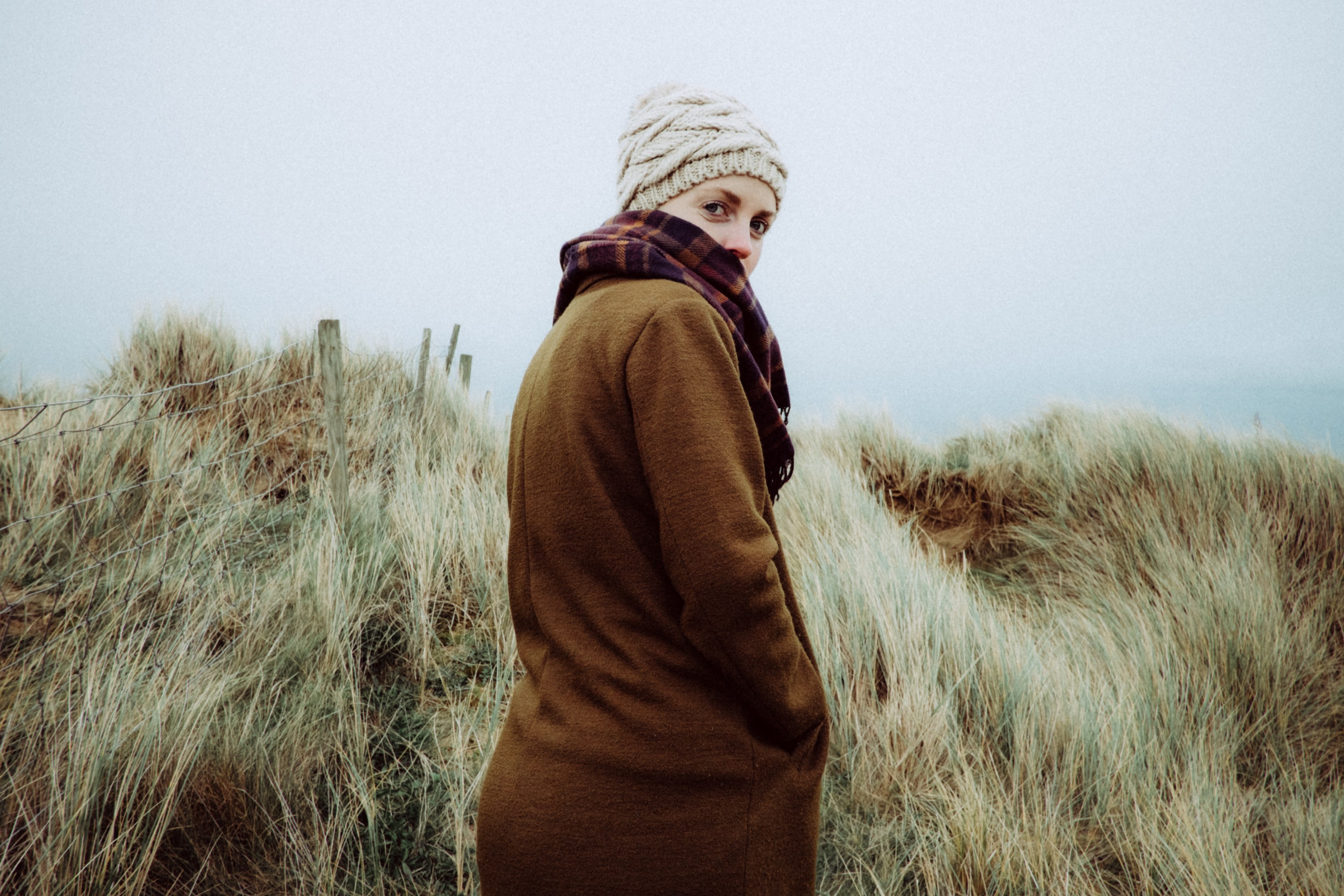 a woman in a knit cap and sweater turns toward the camera among coastal dunes, woman with coastal dunes 4k, HD Wallpaper