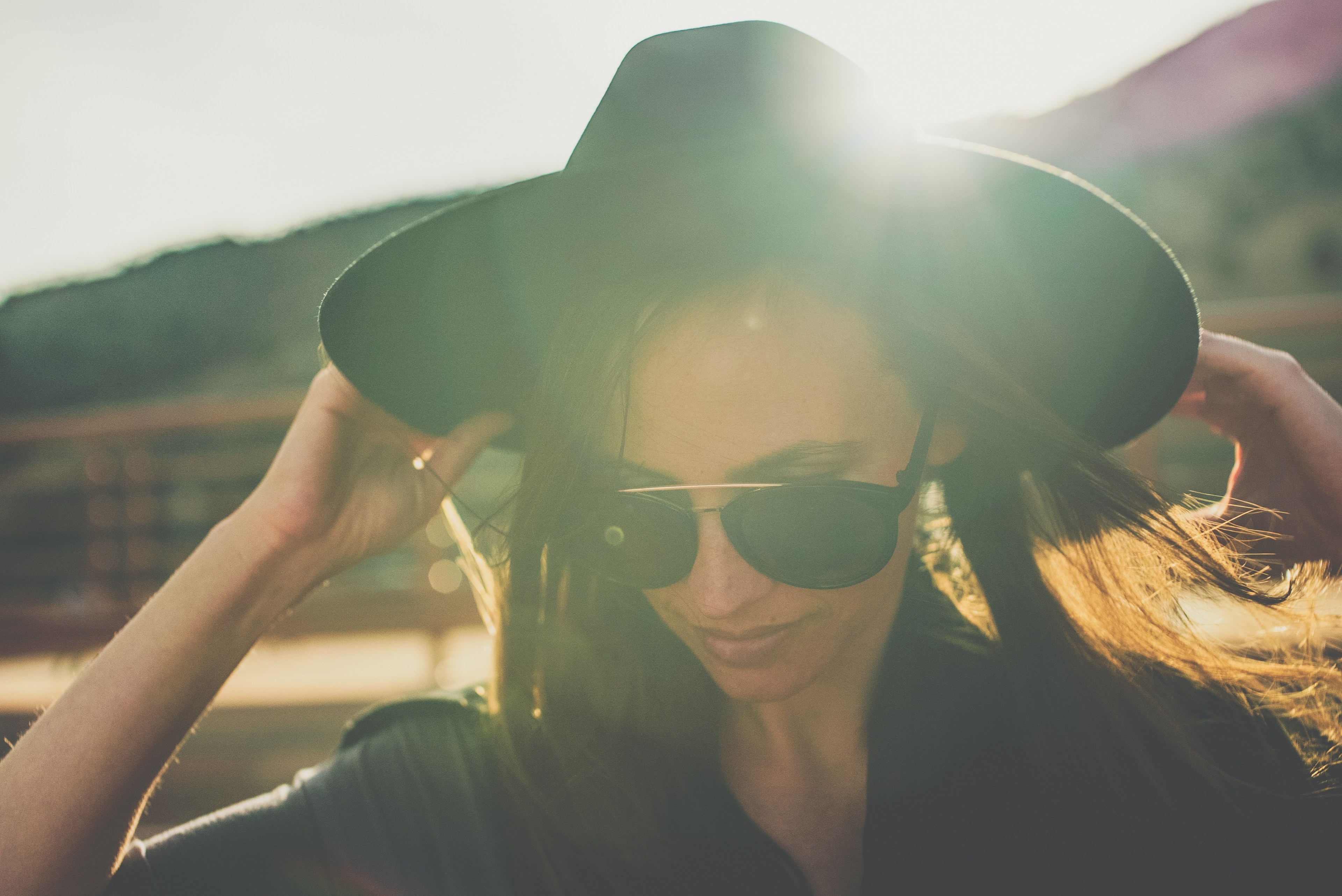 a woman in sunglasses holds the brim of her black hat with sunlight shining behind her, a new hat_ 4k, HD Wallpaper