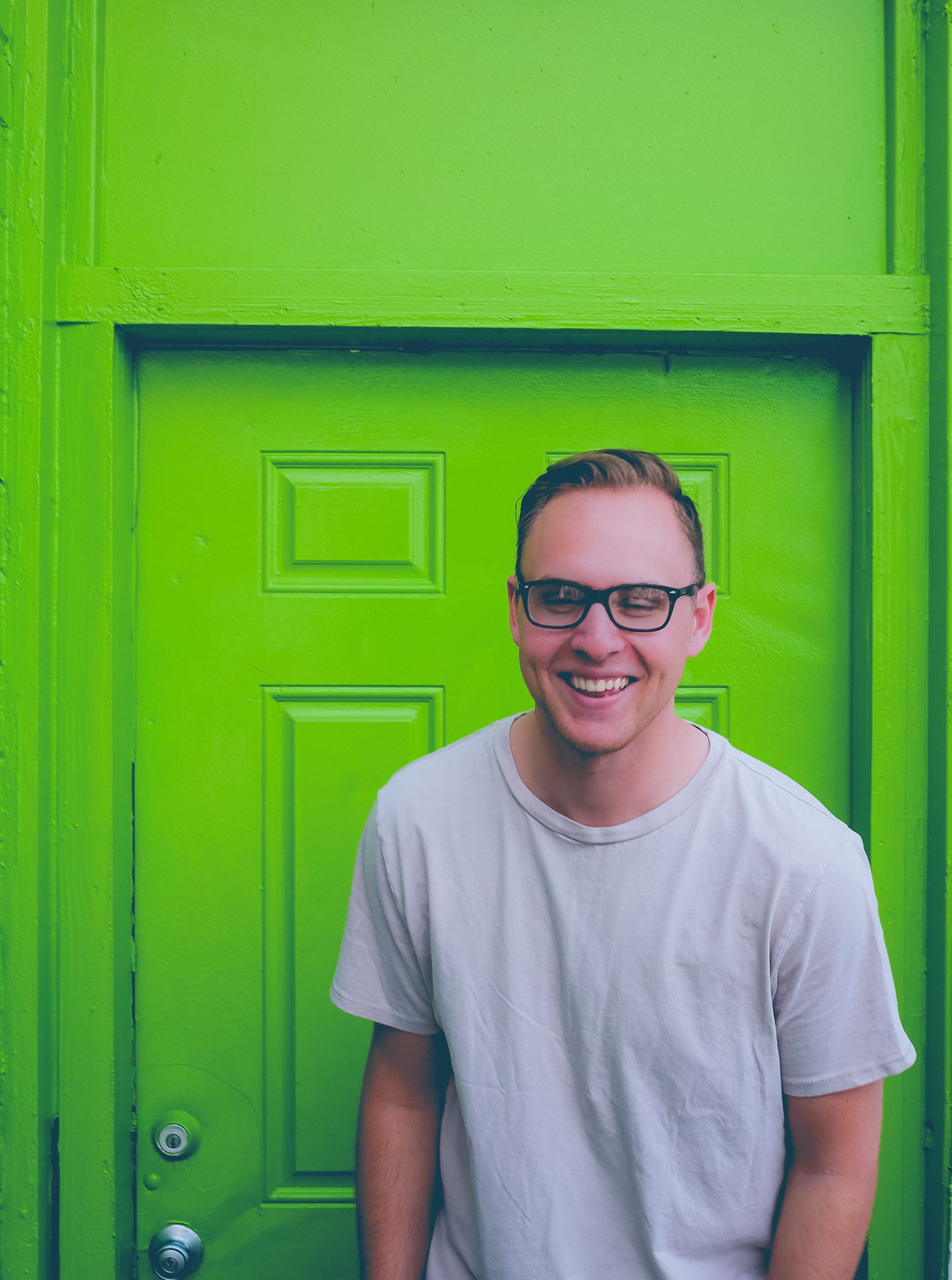 a man wearing glasses smiling while standing in front of a green door, _man in front of green door 4k, Phone HD Wallpaper