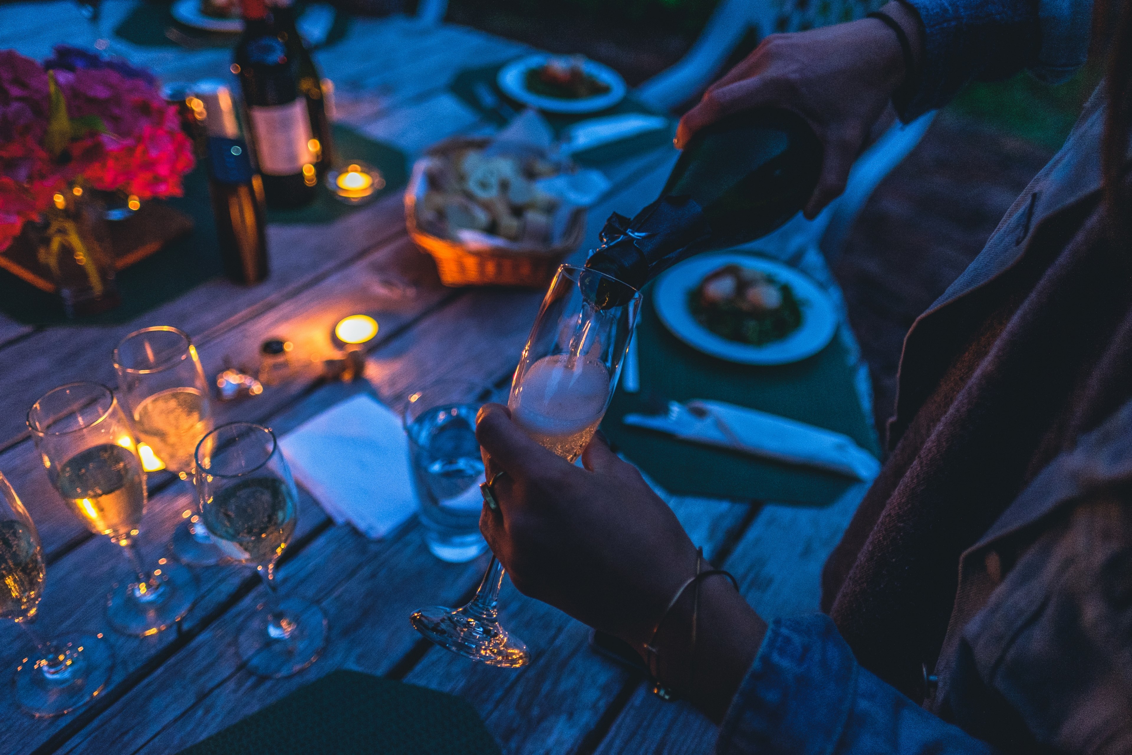 a person pouring champagne into a tall glass at a large outdoor table in the evening, outdoor champagne in the evening 4k, HD Wallpaper