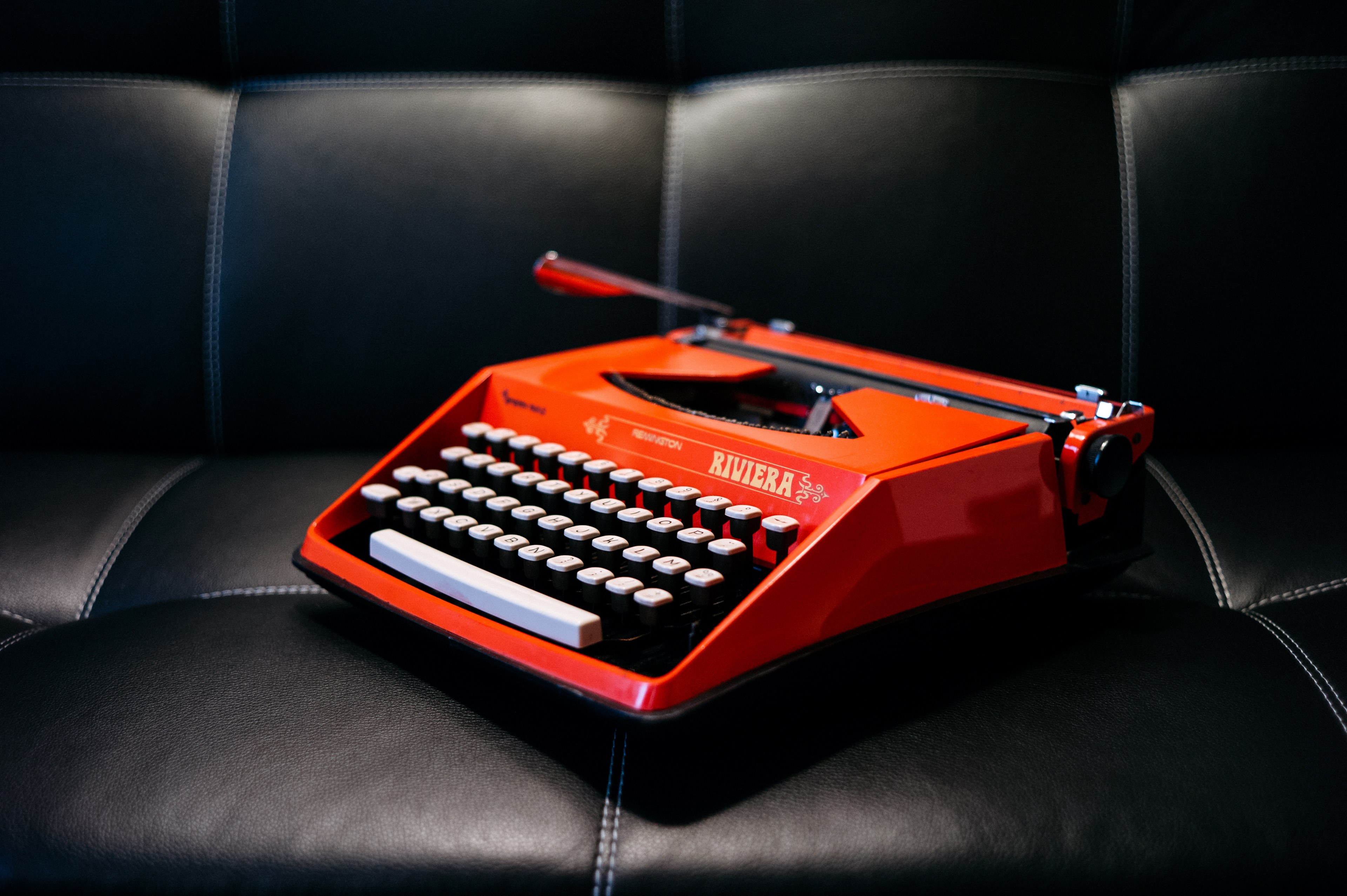 a red riviera typewriter on a black leather couch, red typewriter on black 4k, HD Wallpaper