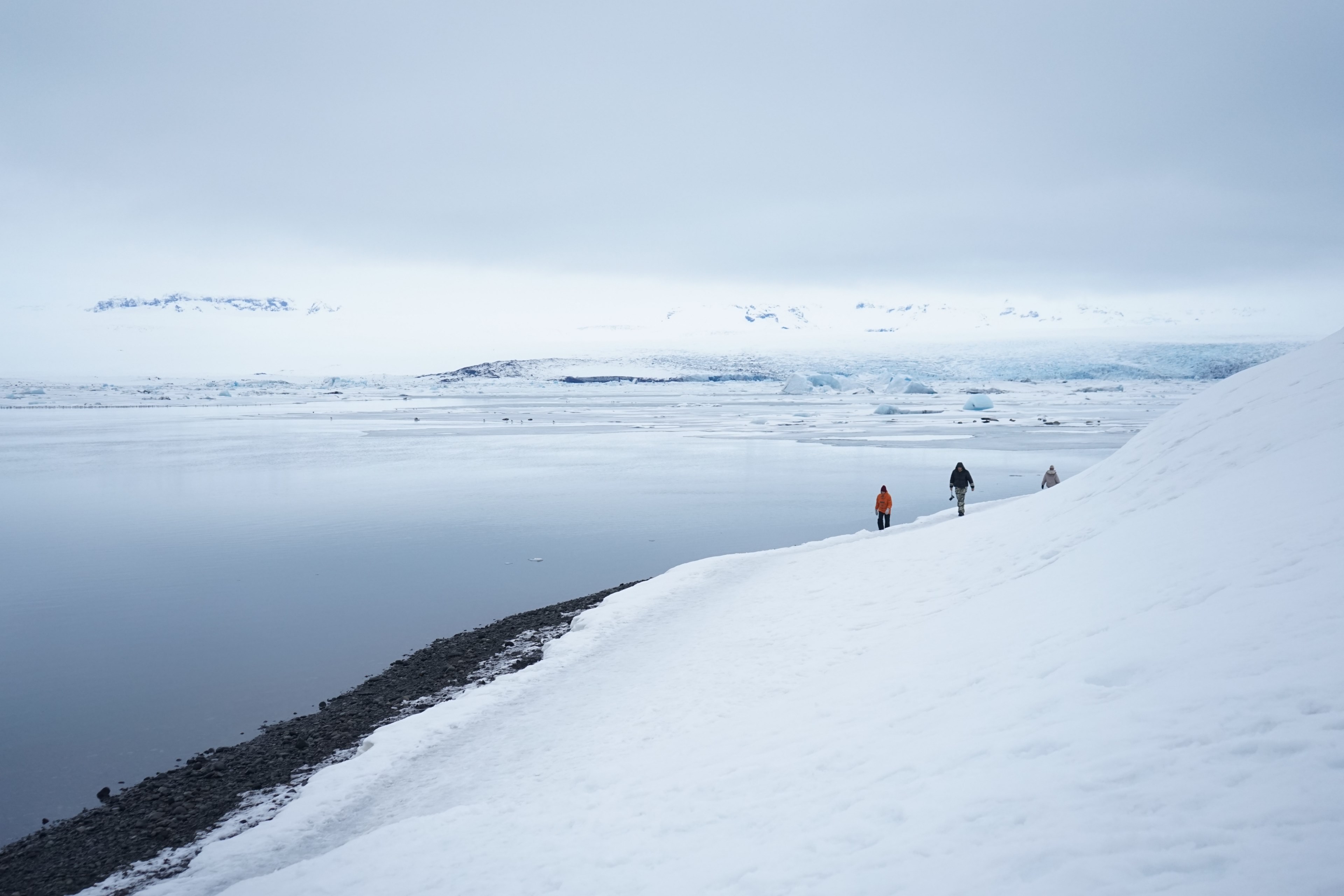 people walking along the bottom of a snowy mountain near an ocean, walking winter mountains 4k, HD Wallpaper